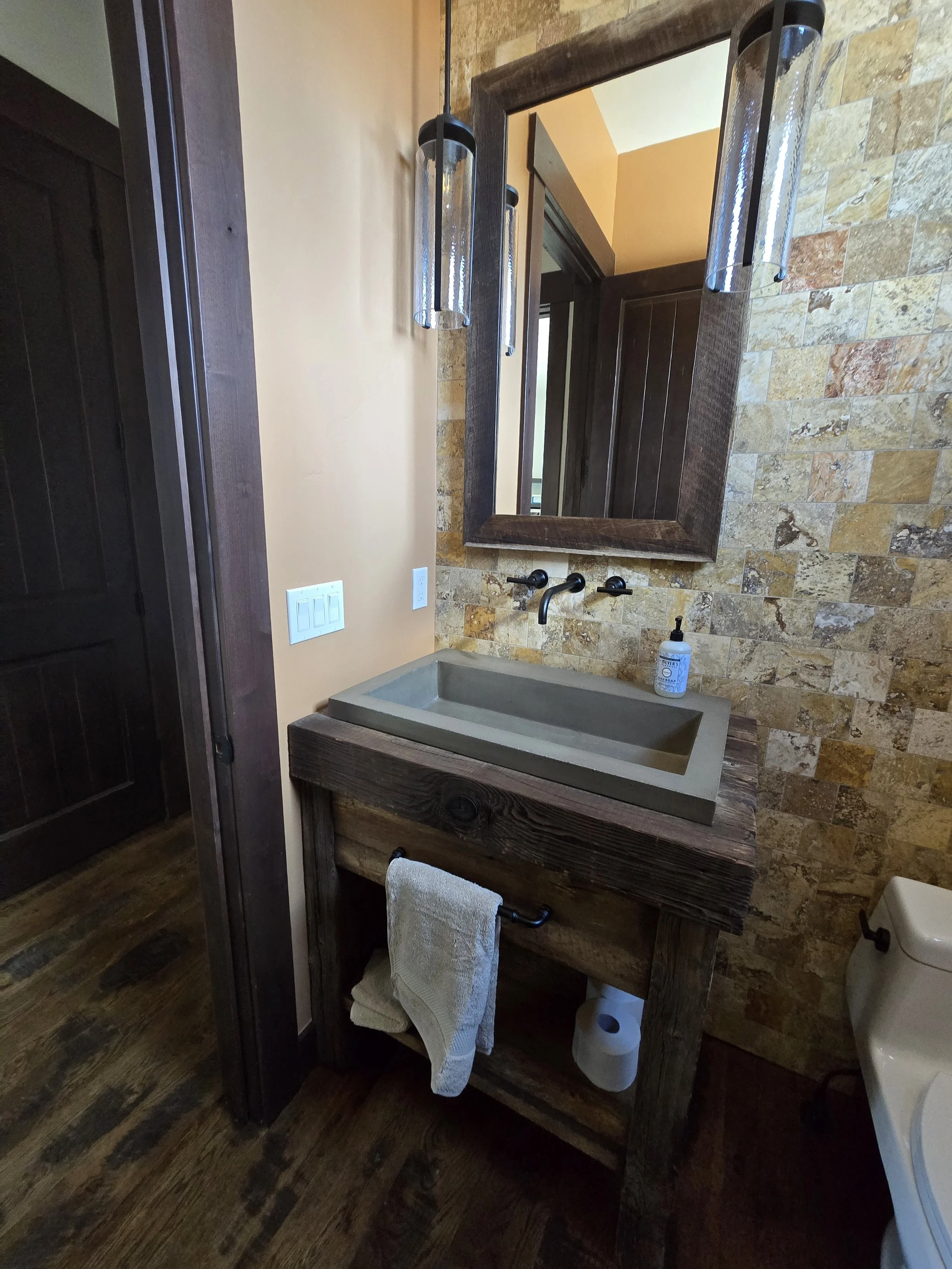Rustic reclaimed wood vanity with five-inch thick countertop, stone vessel sink, matching oversized wall mirror, and open shelving—custom furniture-style cabinetry design