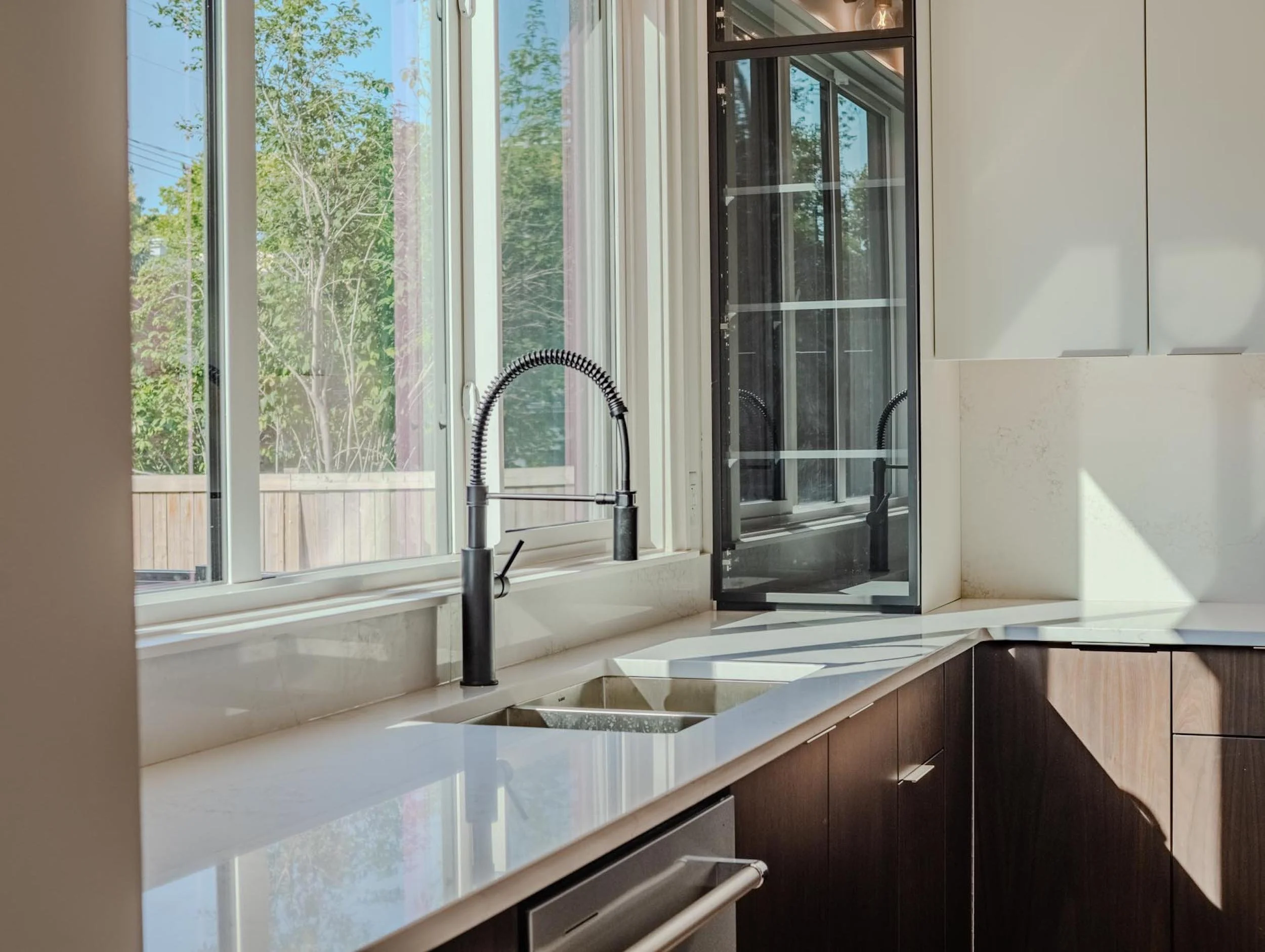 Modern kitchen detail in Belgravia featuring a black designer faucet and quartz countertops with views of mature Edmonton greenery.