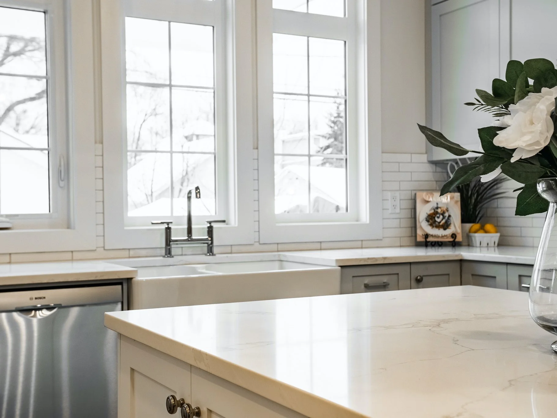 Kohler Purist bridge faucet and Franke Manor House fireclay apron front sink paired with white cabinetry.