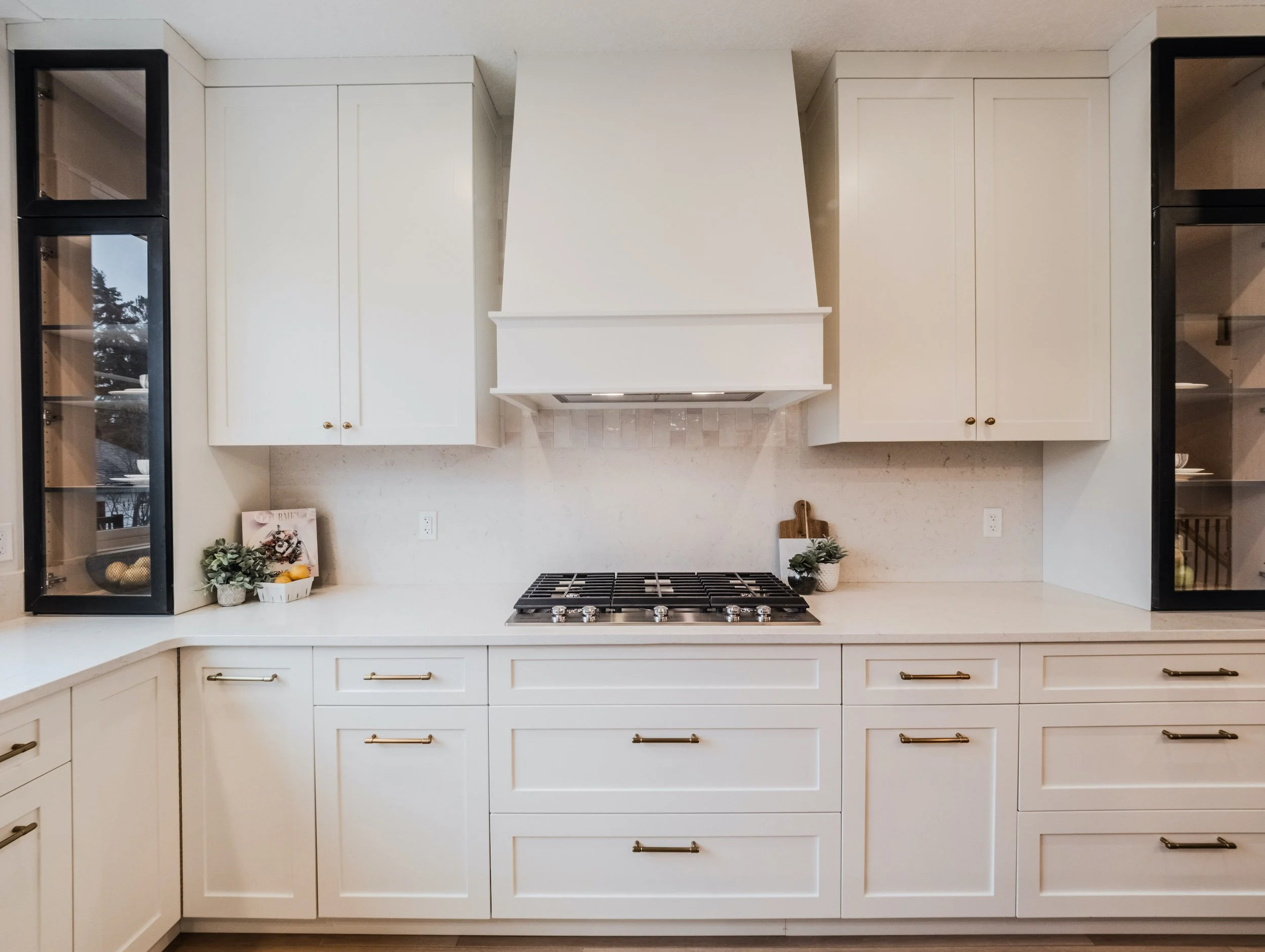 Sleek white-on-white kitchen with professional gas range, integrated hood, and quartz backsplash.
