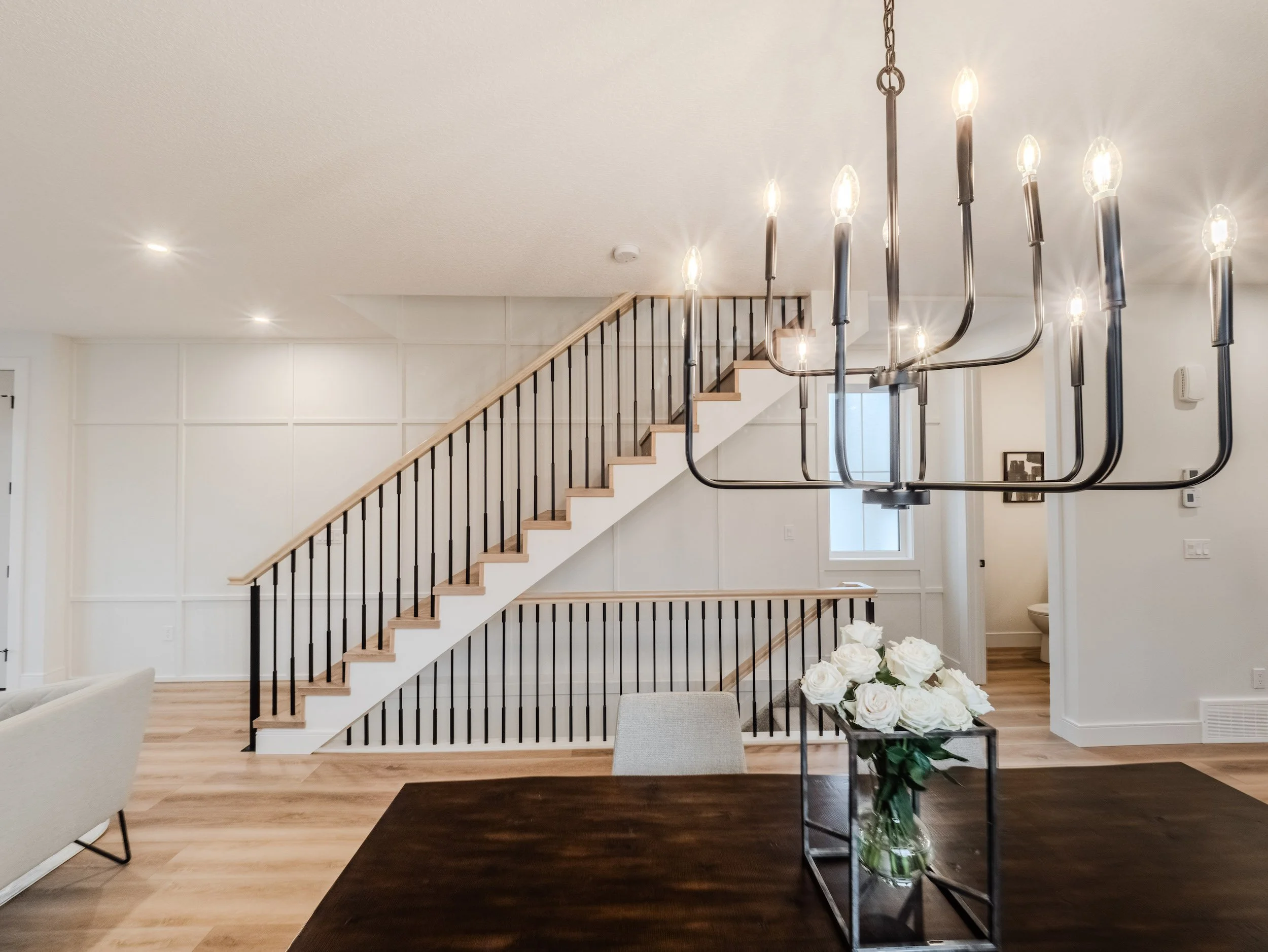 Custom eastern stringer staircase featuring luxury iron post and rod railings, extensive custom millwork detailing on the staircase wall, and a large multi-tiered modern chandelier.