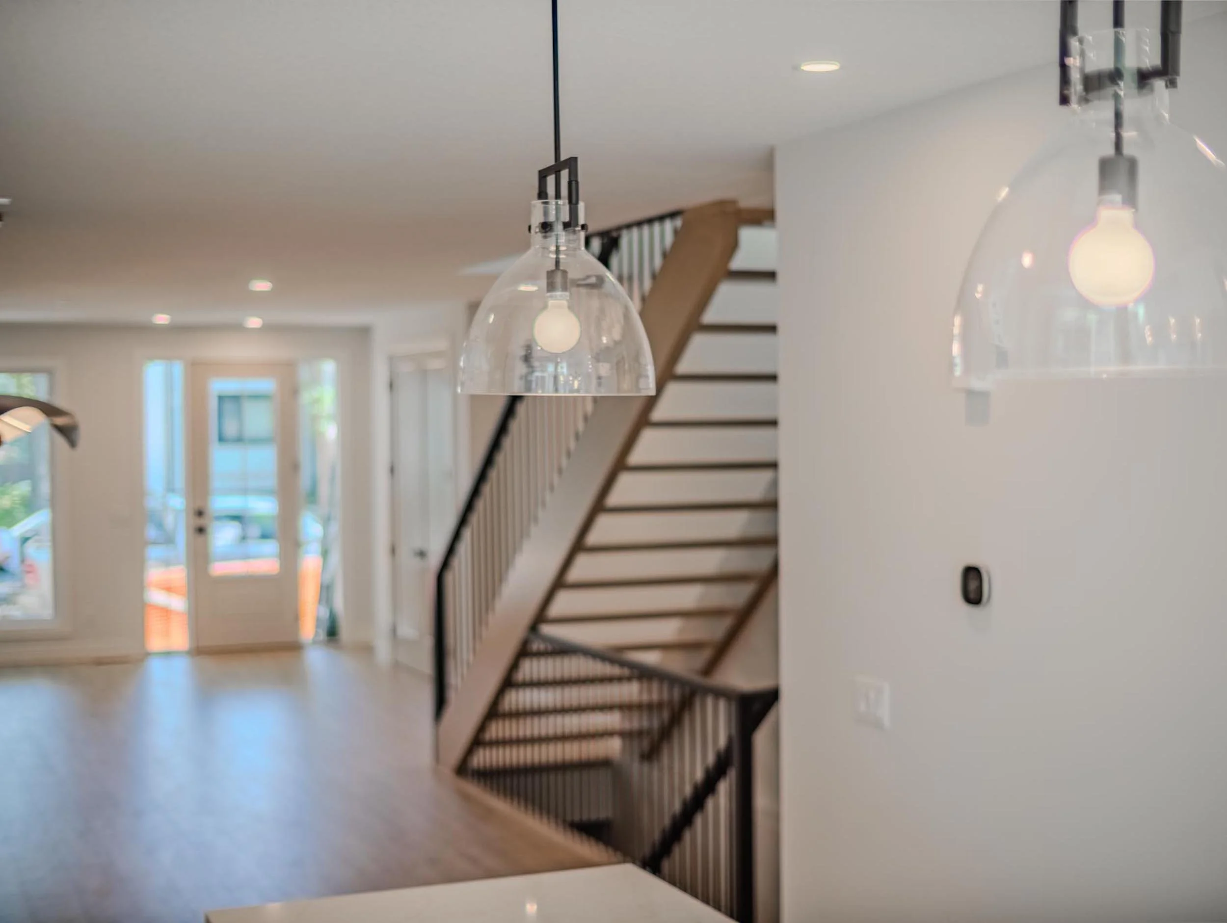 Bright modern entryway showing the central open-riser staircase and warm wood flooring.