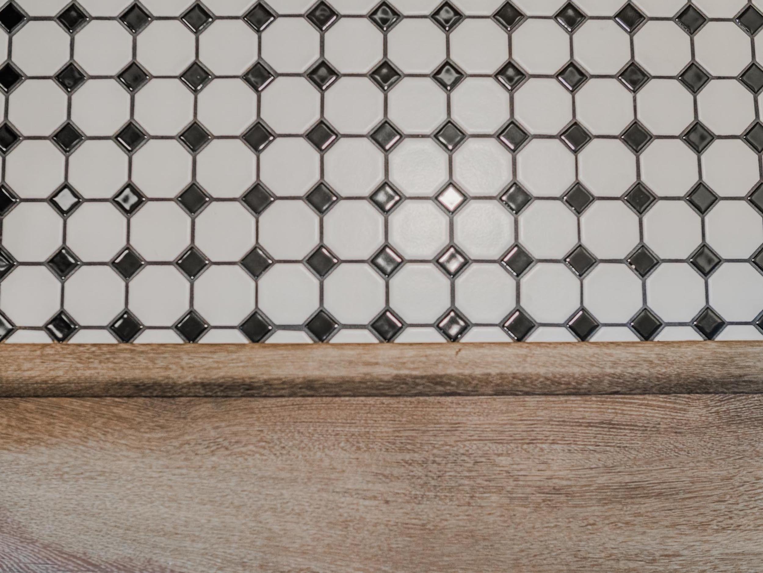 Intricate black and white mosaic tile detail meeting a natural wood transition in a high-end custom home.