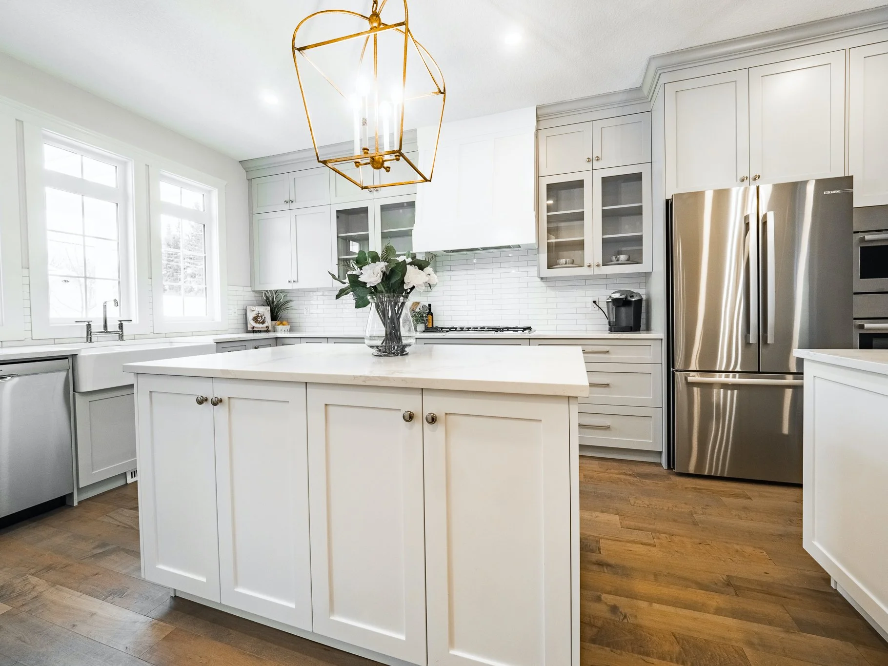 Airy kitchen featuring white islands, soft grey cabinets, and Chapman & Myers Stonington lanterns in antique gild.