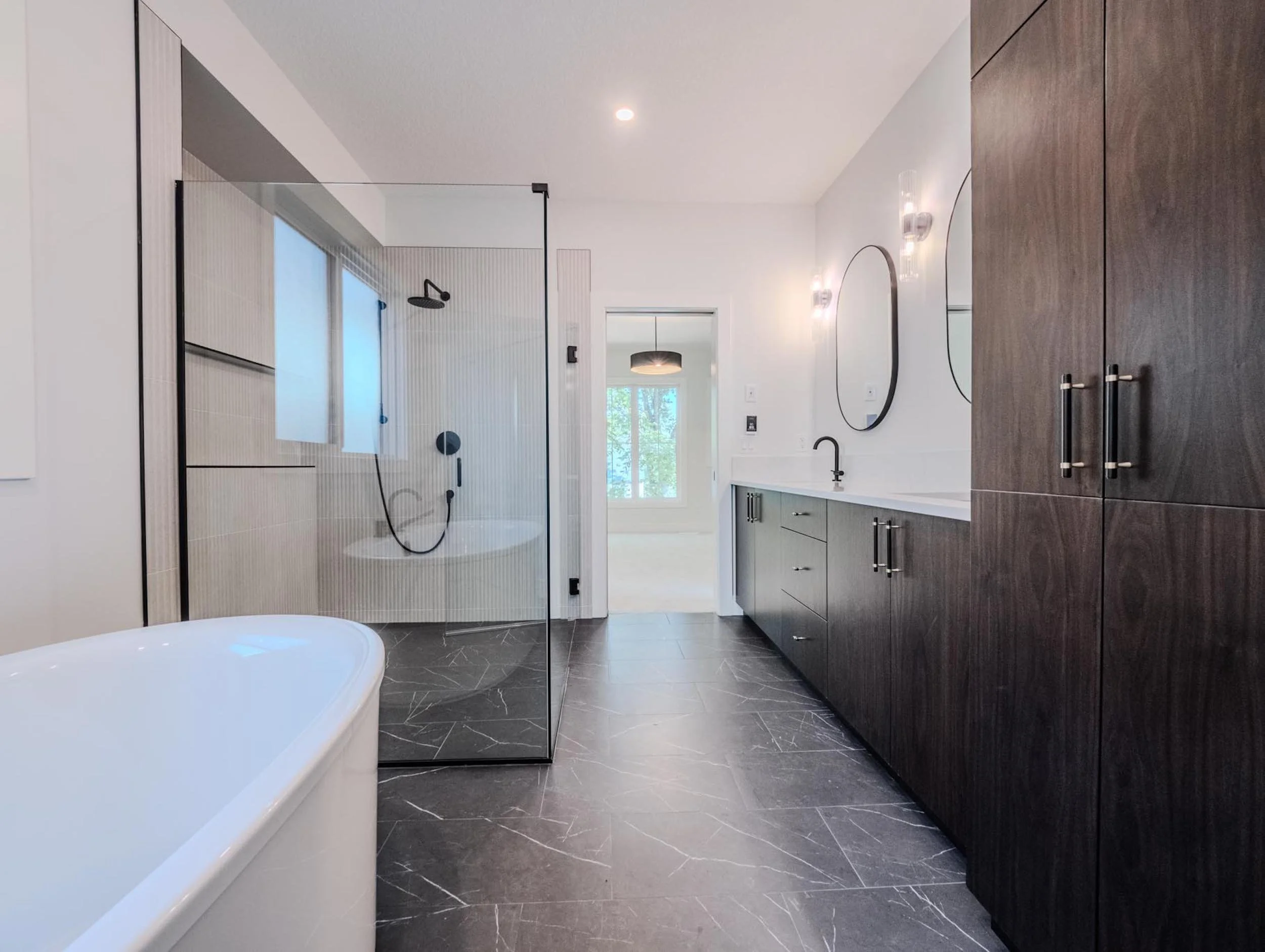 Spacious modern primary bathroom with black tile flooring, a freestanding soaking tub, and a glass-enclosed curbless shower.