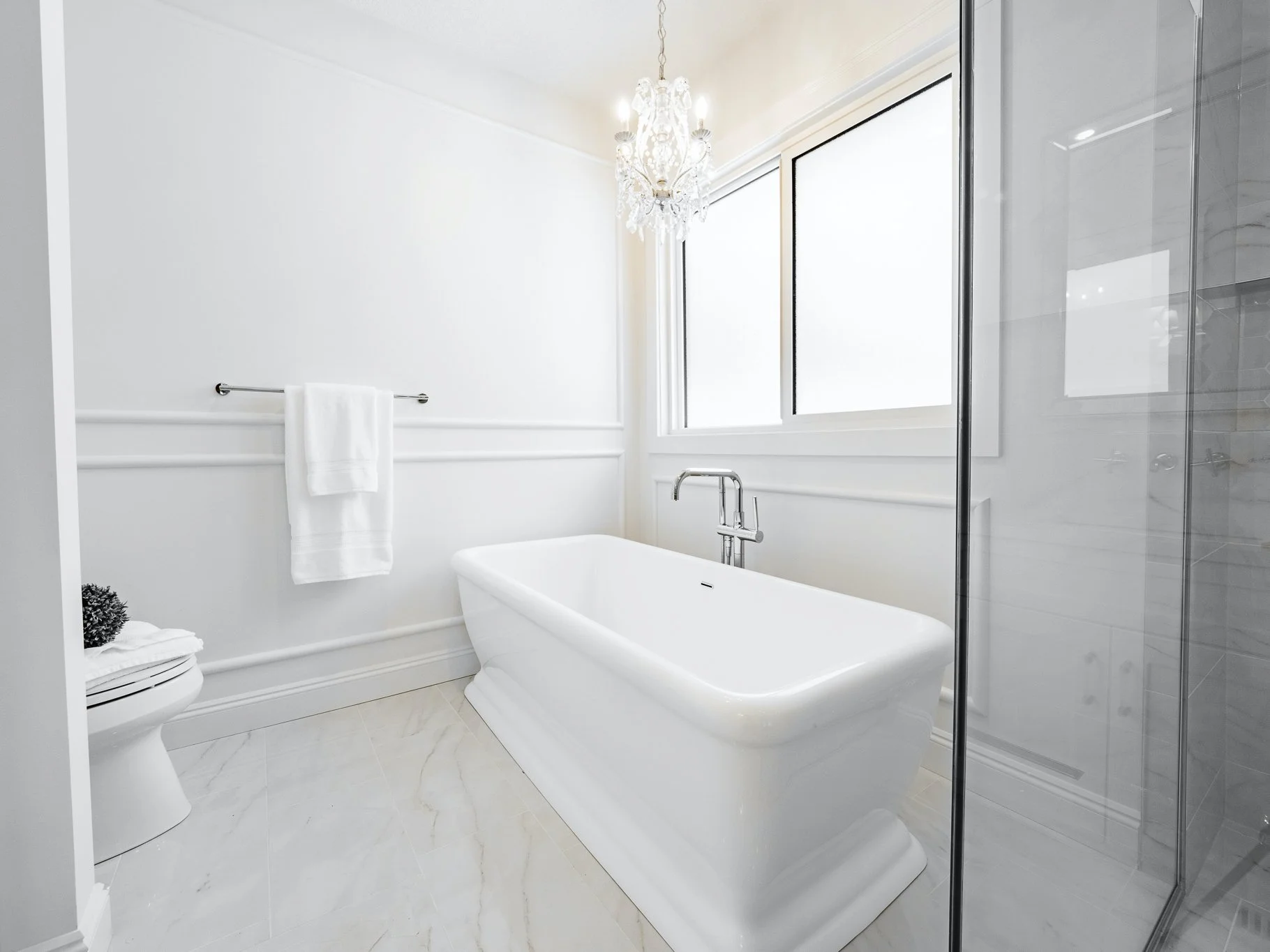 Freestanding soaking tub with a Kohler Purist floor-mounted filler and a Restoration Hardware Aislynn crystal chandelier.