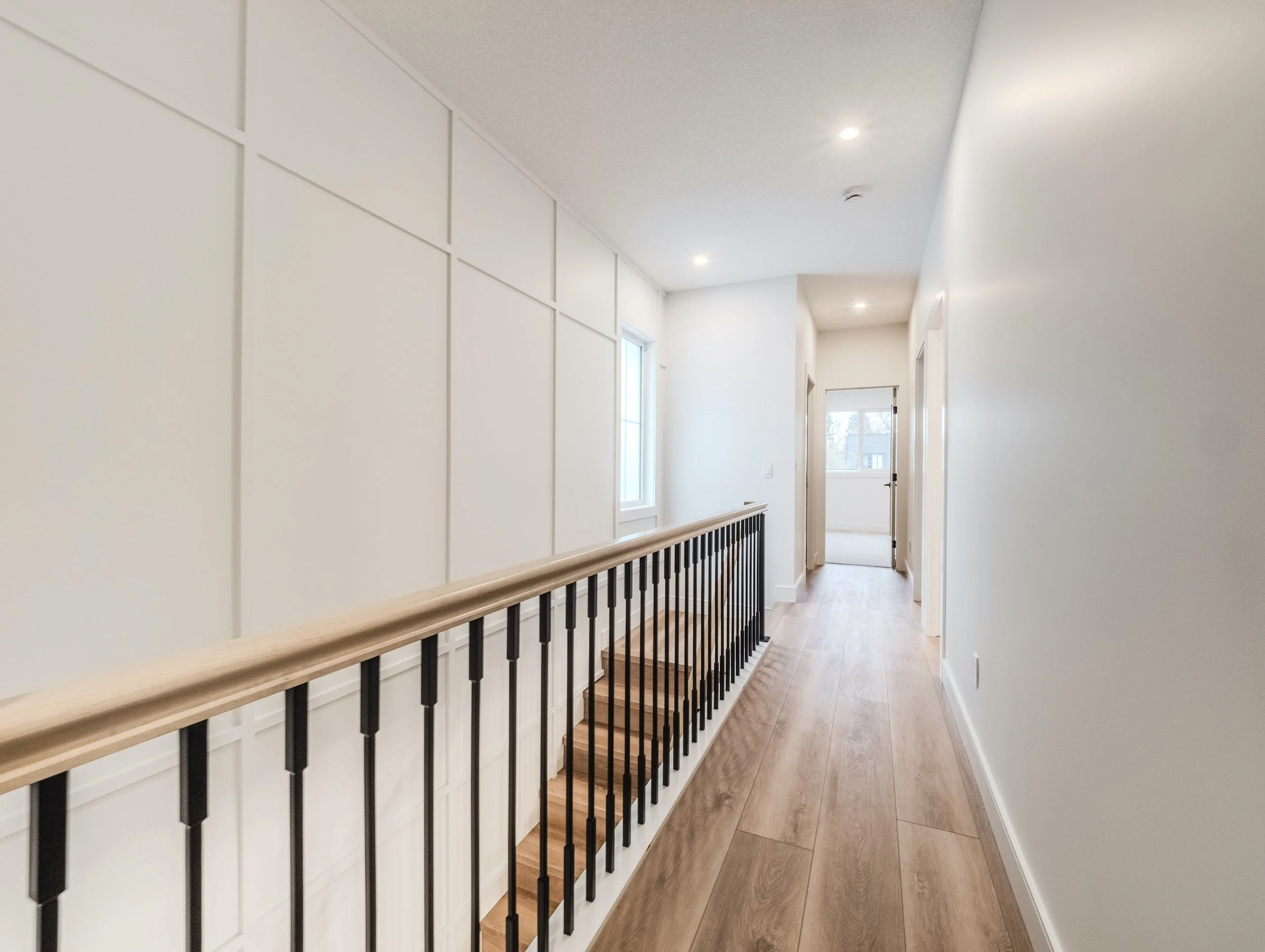 Sunlit upper level landing and hallway with continuous iron rod railing and extensive custom millwork detailing on the staircase wall.
