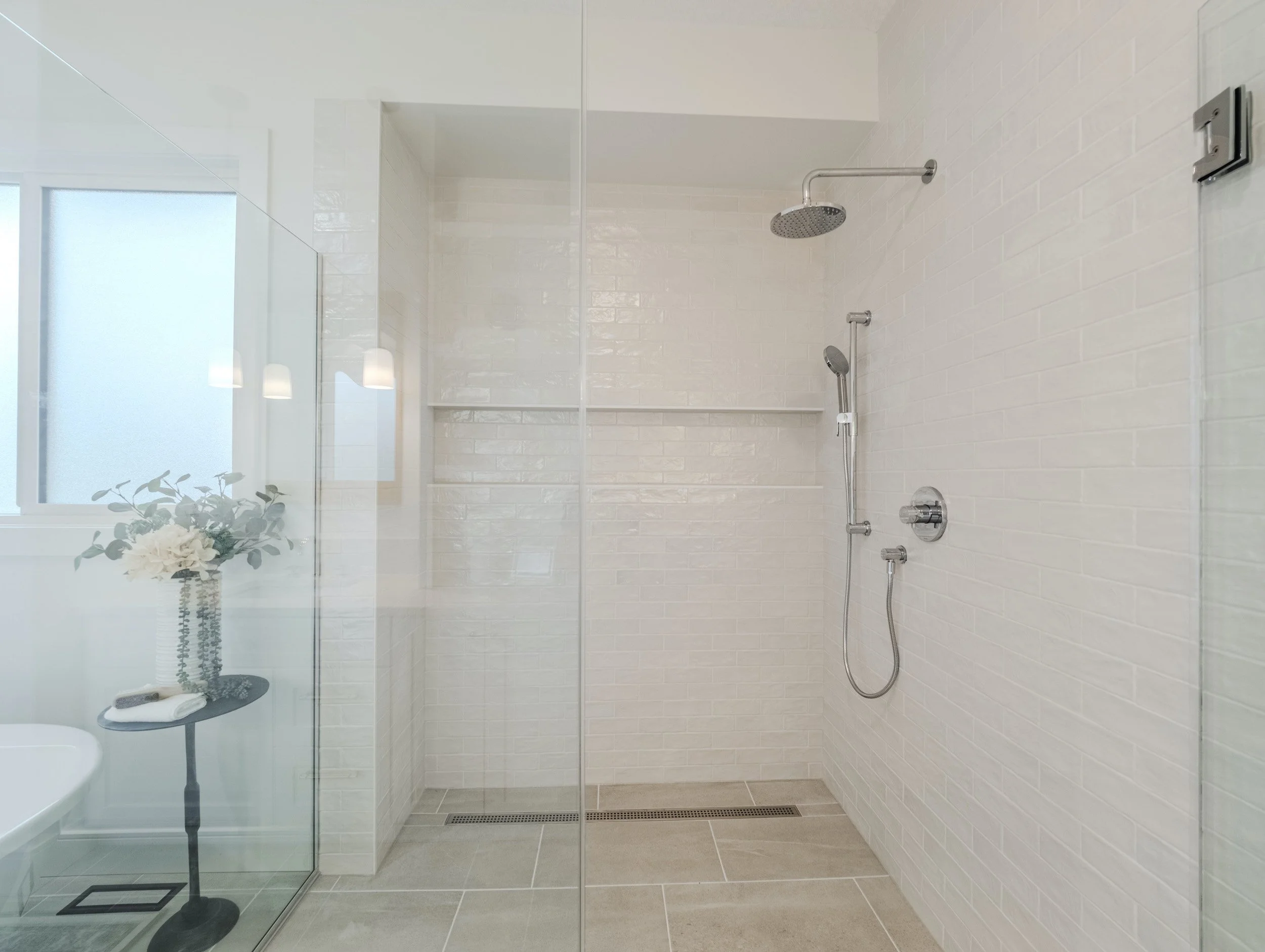 Spa-inspired primary ensuite bathroom showing the custom curbless tiled shower and large window.