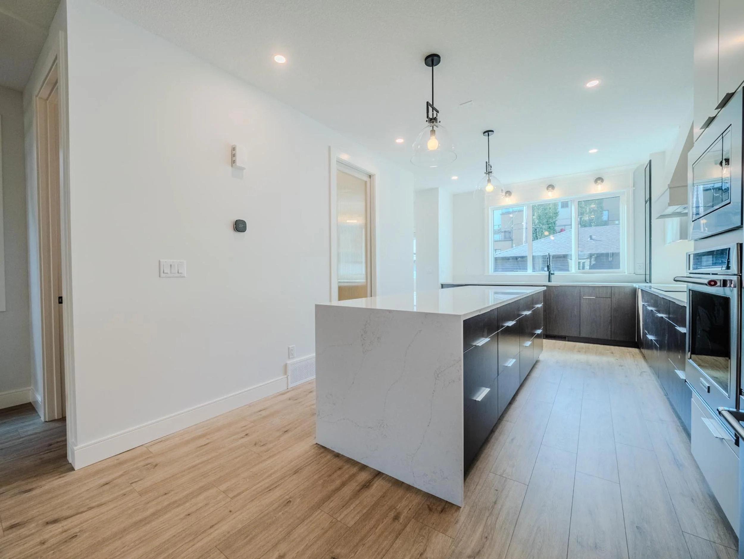 Open-concept kitchen with a large waterfall island and warm walnut cabinetry in a modern Edmonton infill.