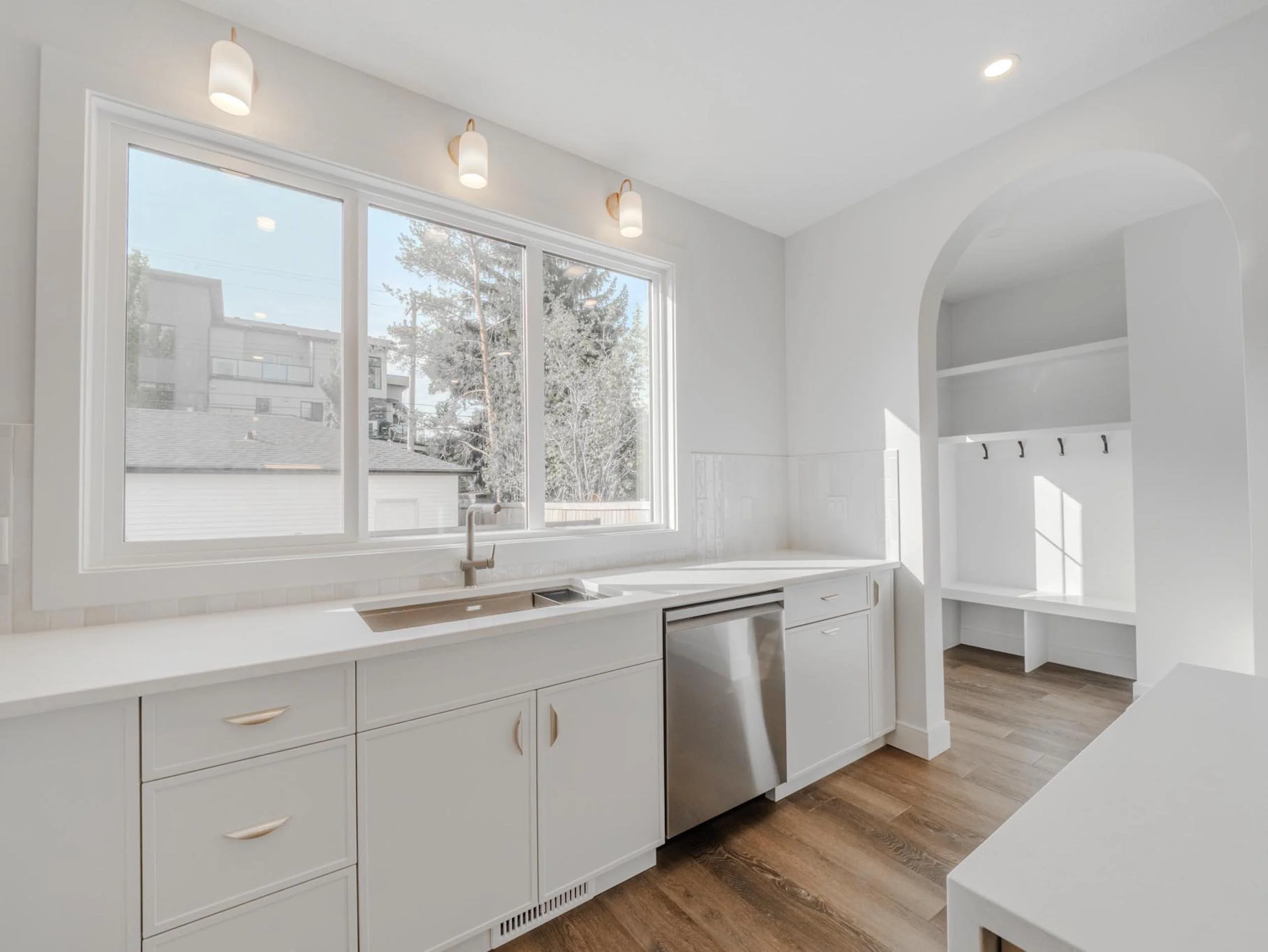 Bright minimalist kitchen with built-in cabinetry, modern over-window wall sconces, and a Franke Fragranite workstation sink with a coordinating high-performance faucet.