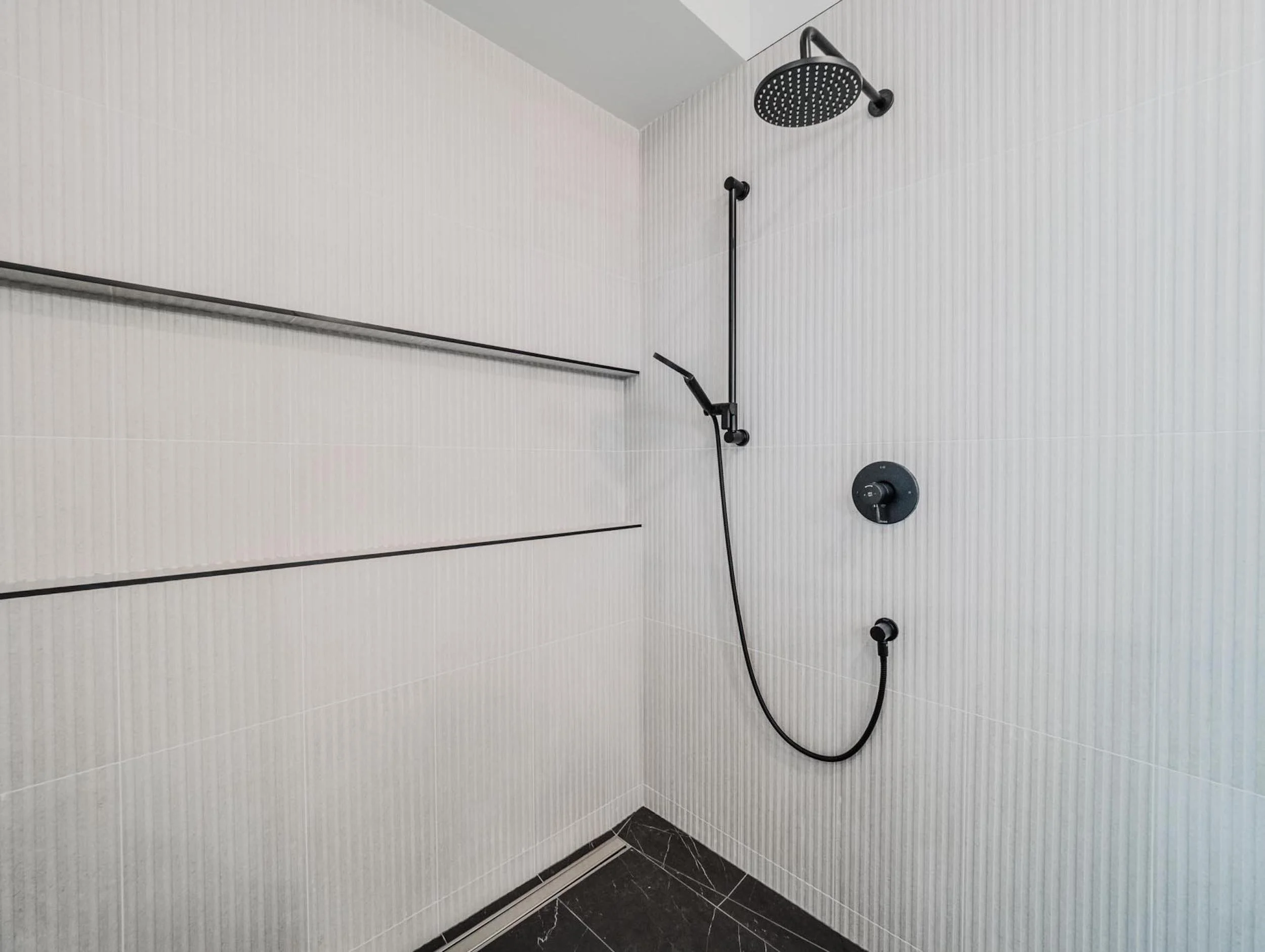 Close-up of a curbless shower with vertical stacked tile and matte black fixtures.