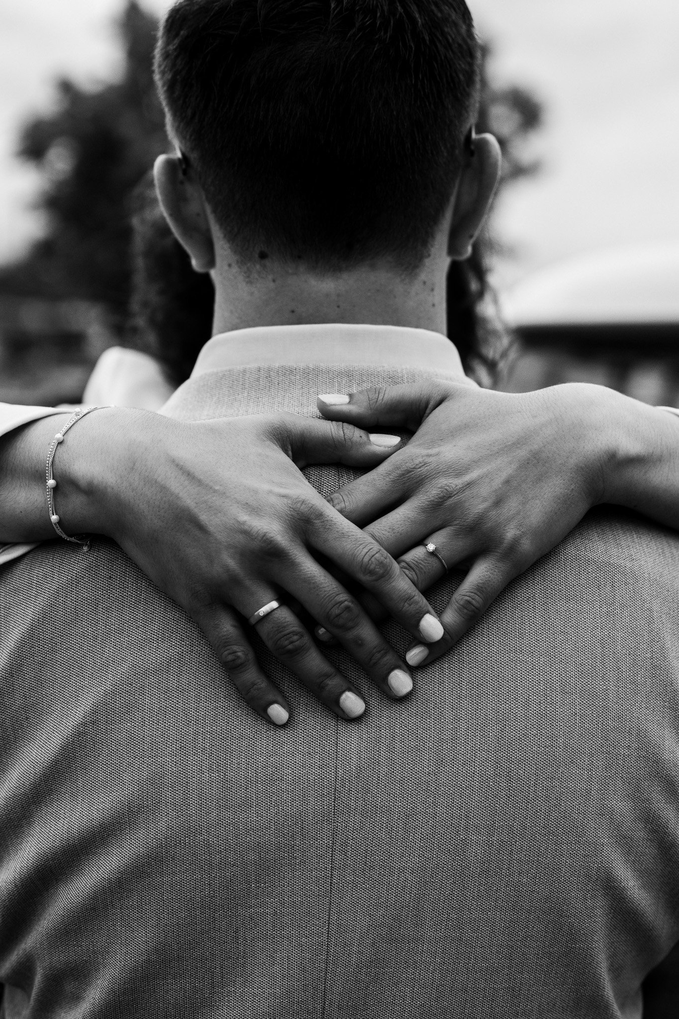 Black and white photo of a man seen from behind, with a woman's hands resting on his shoulders.