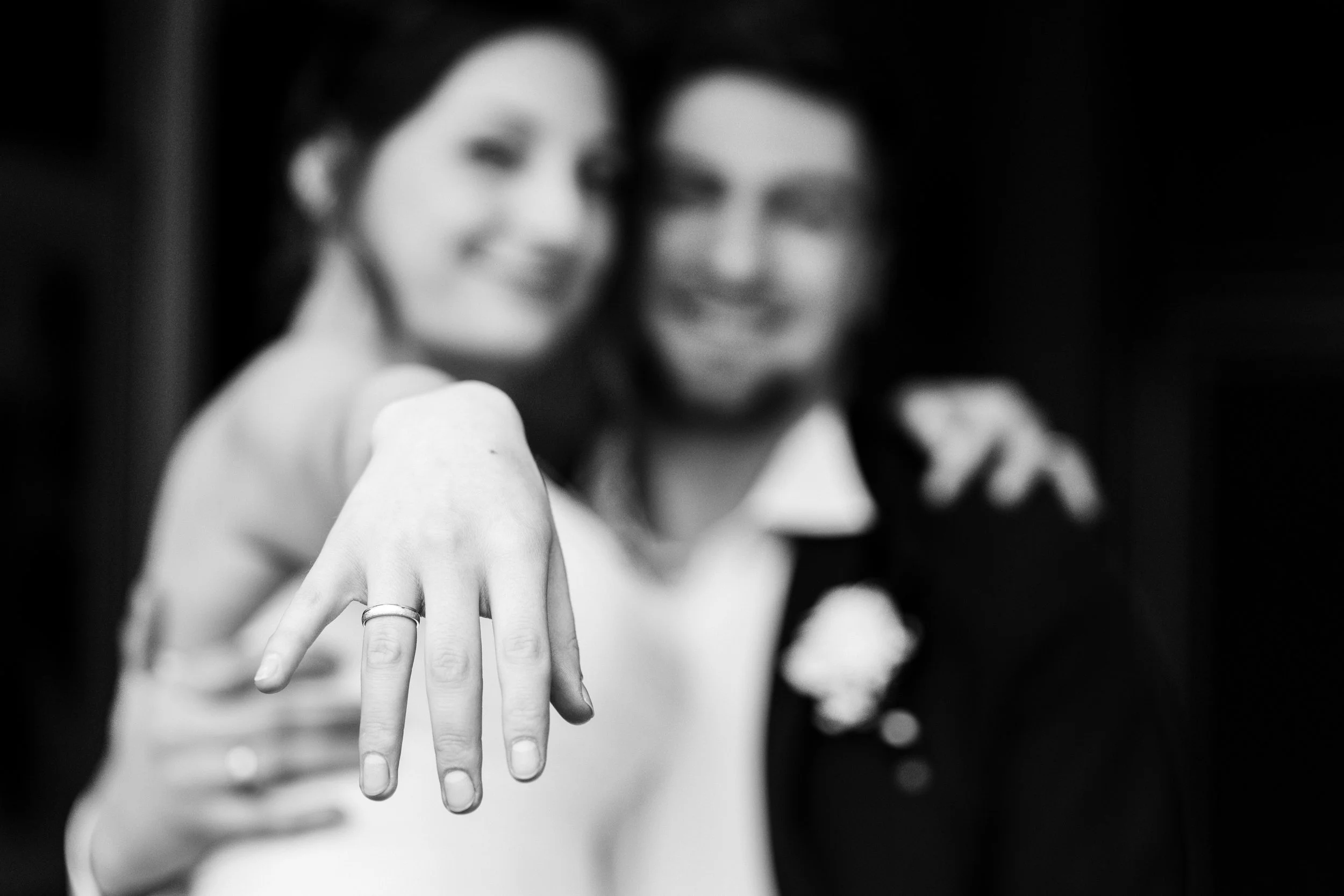 A couple smiling, with the woman showing off her wedding ring on her left hand in a close-up shot, black and white photo.