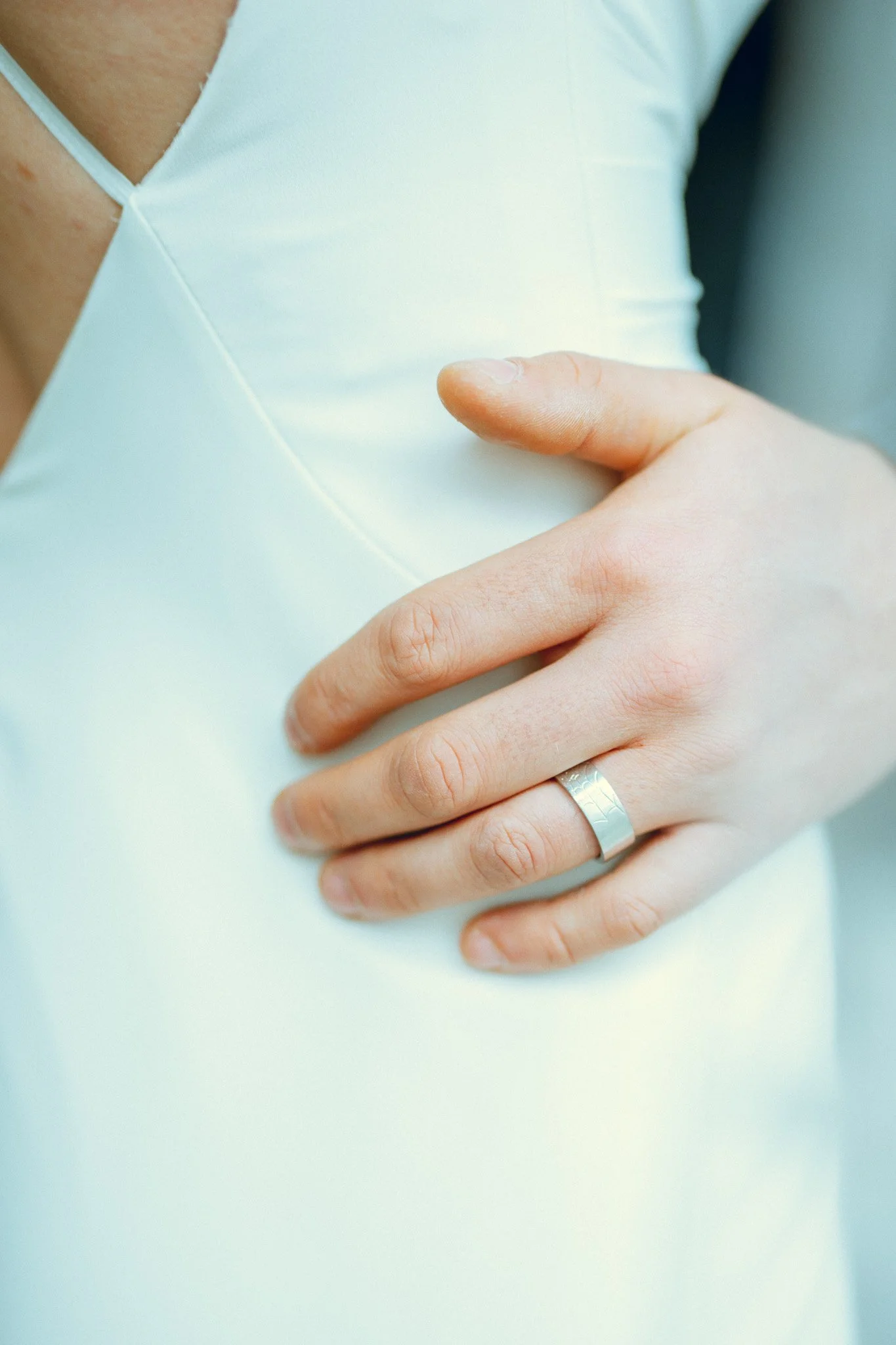 Close-up of a person wearing a white dress with their hand on their chest, showing a silver ring on their ring finger.