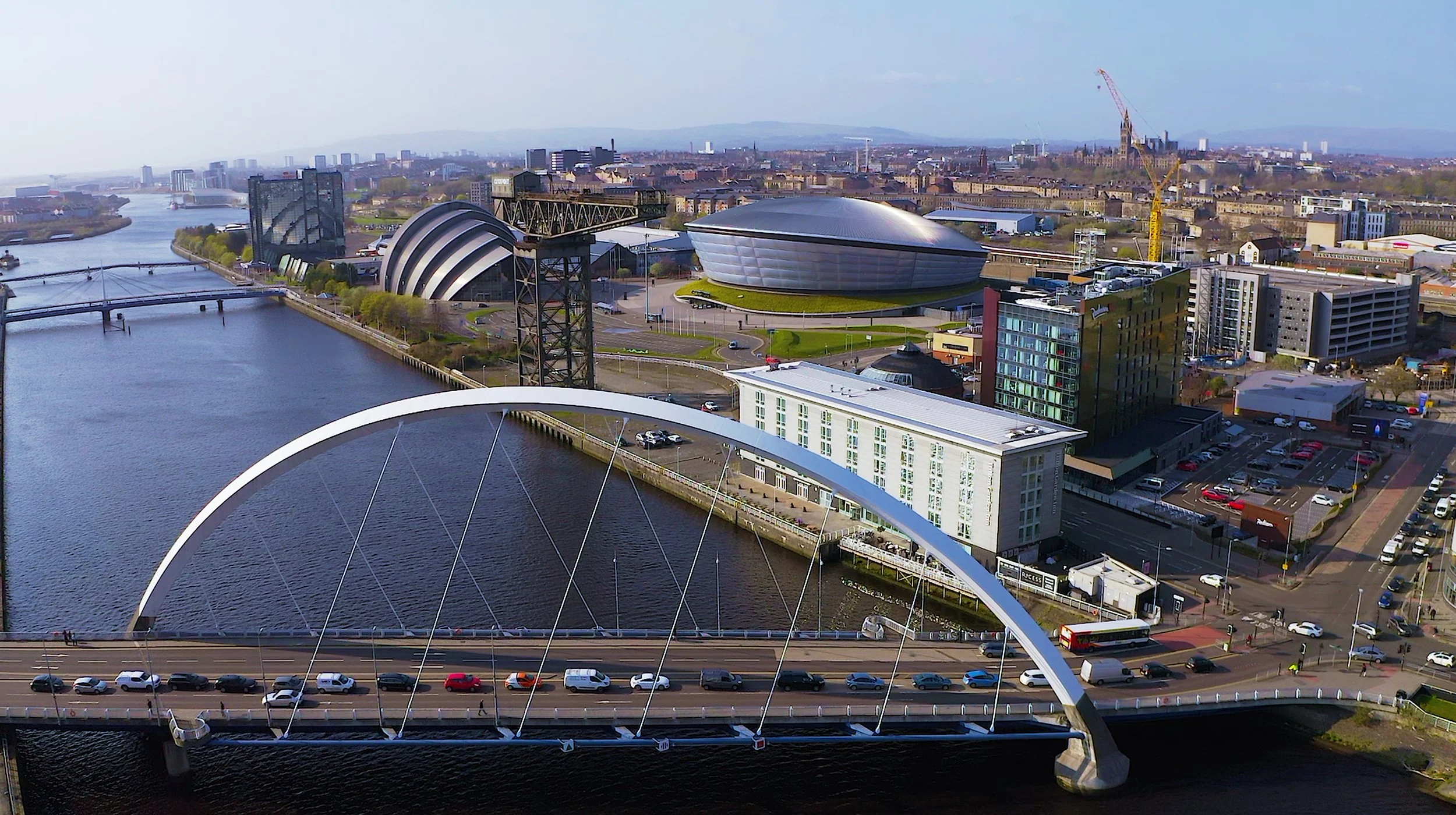 Aerial view of a cityscape with a river, modern buildings, and a large white arch bridge crossing over the river.