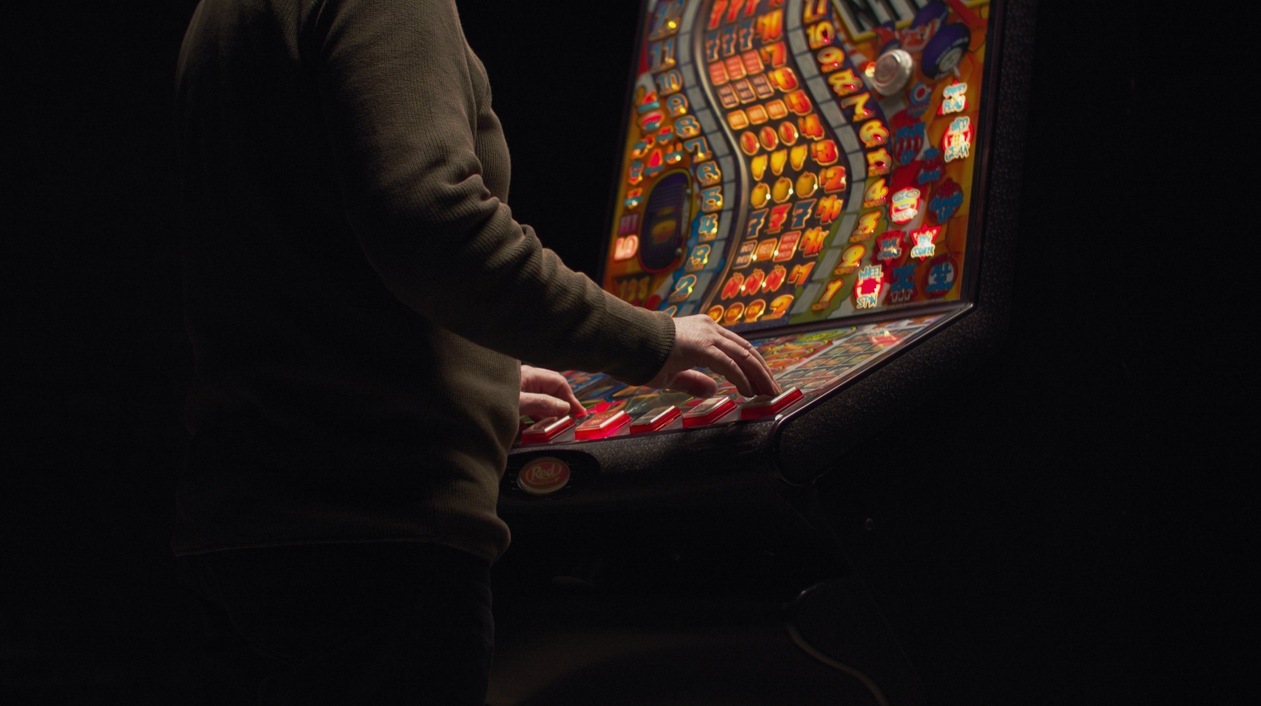 Person playing on a brightly lit slot machine in a dark arcade or casino setting.