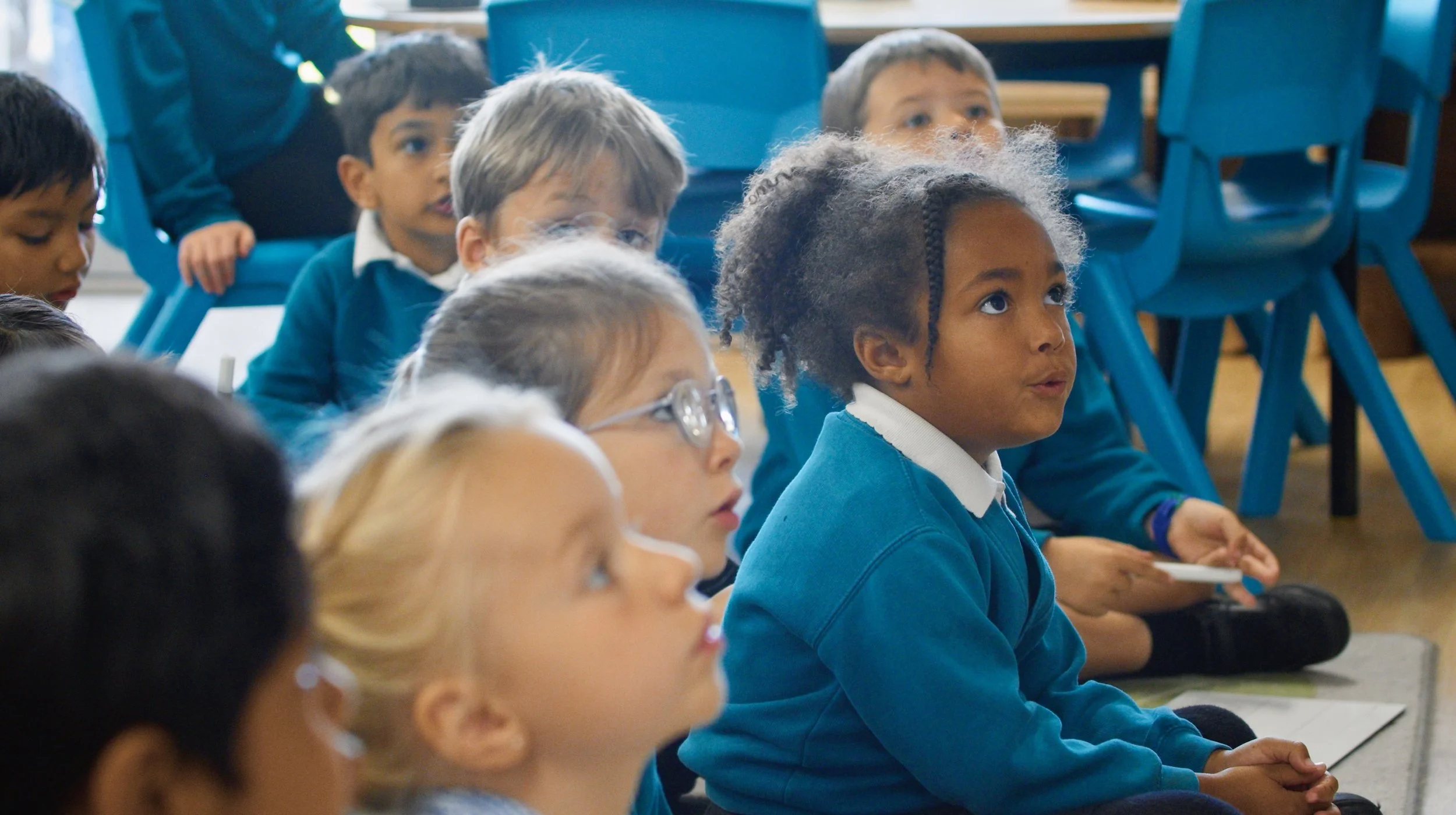 Group of young school children sitting on the floor in a classroom, attentively listening.