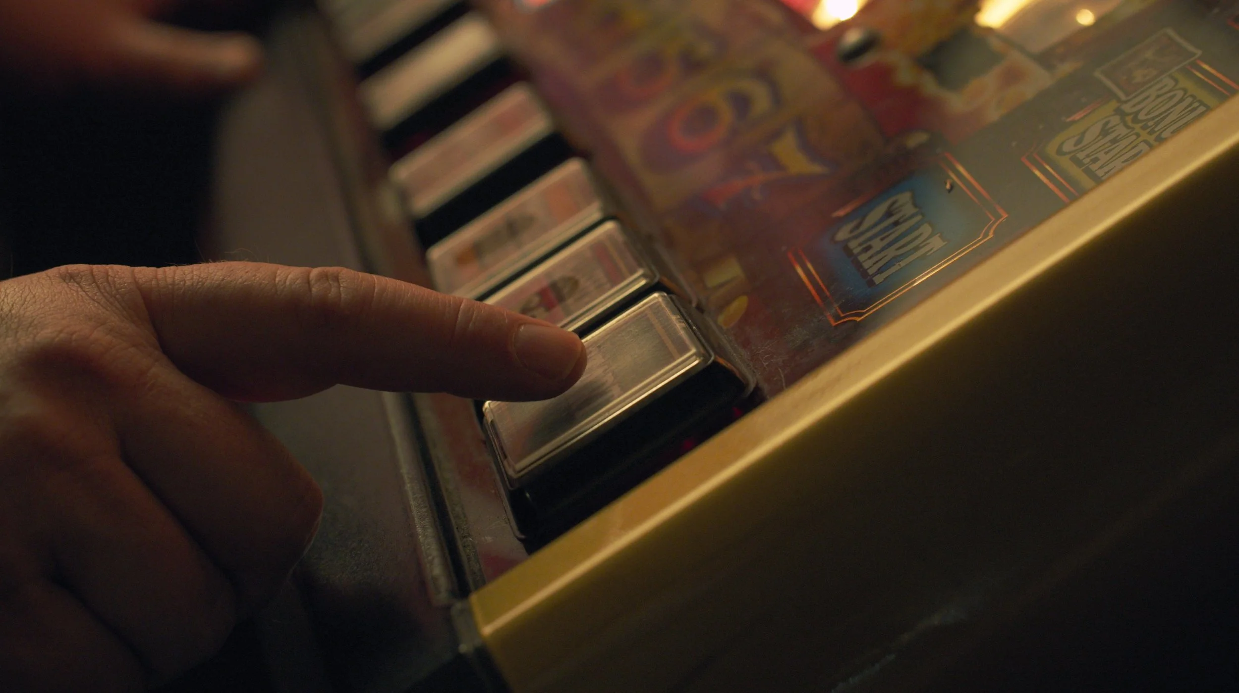 A hand with a finger pressing a button on a vintage jukebox, showing a row of other buttons and colorful artwork on it.