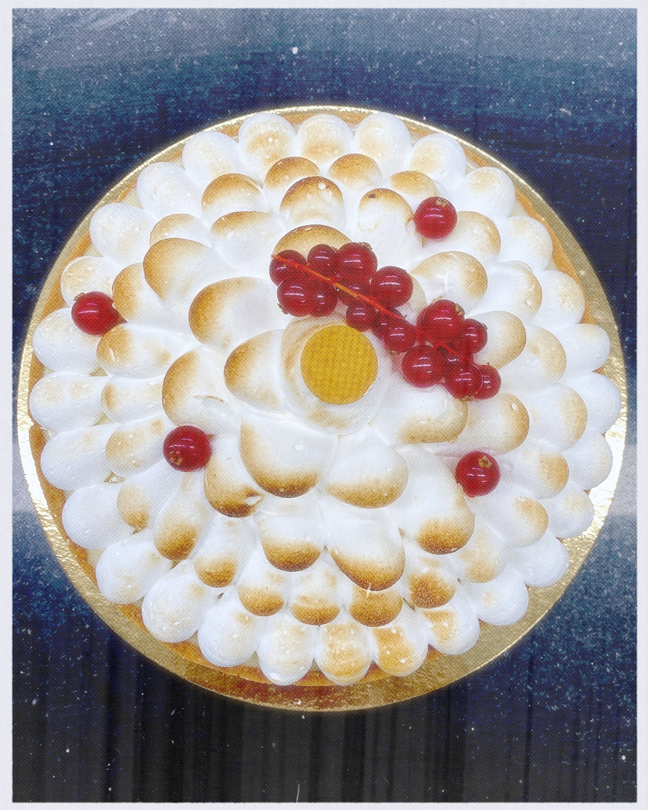 A round cake decorated with white and golden-brown meringue dollops, red currants, and a garnish of redcurrants on top.