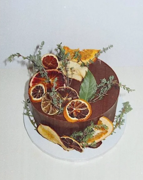 Chocolate cake decorated with dried citrus slices, fresh herbs, and slices of dried fruit.