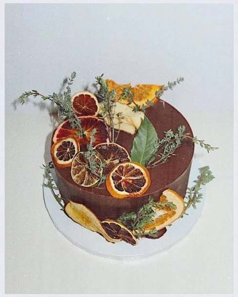 Chocolate cake garnished with dried citrus slices and herbs.