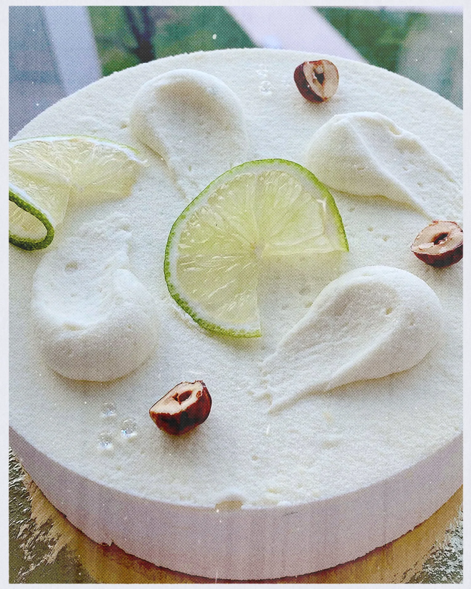 Close-up of a creamy white cake topped with lime slices, dollops of whipped cream, a cherry half, and a thin lime peel.