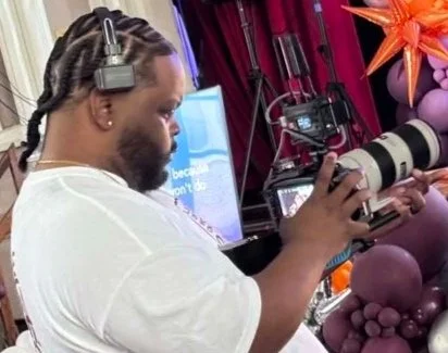Modern house with wooden exterior, stone steps leading up to porch, surrounded by grassy landscape, mountain range in background.