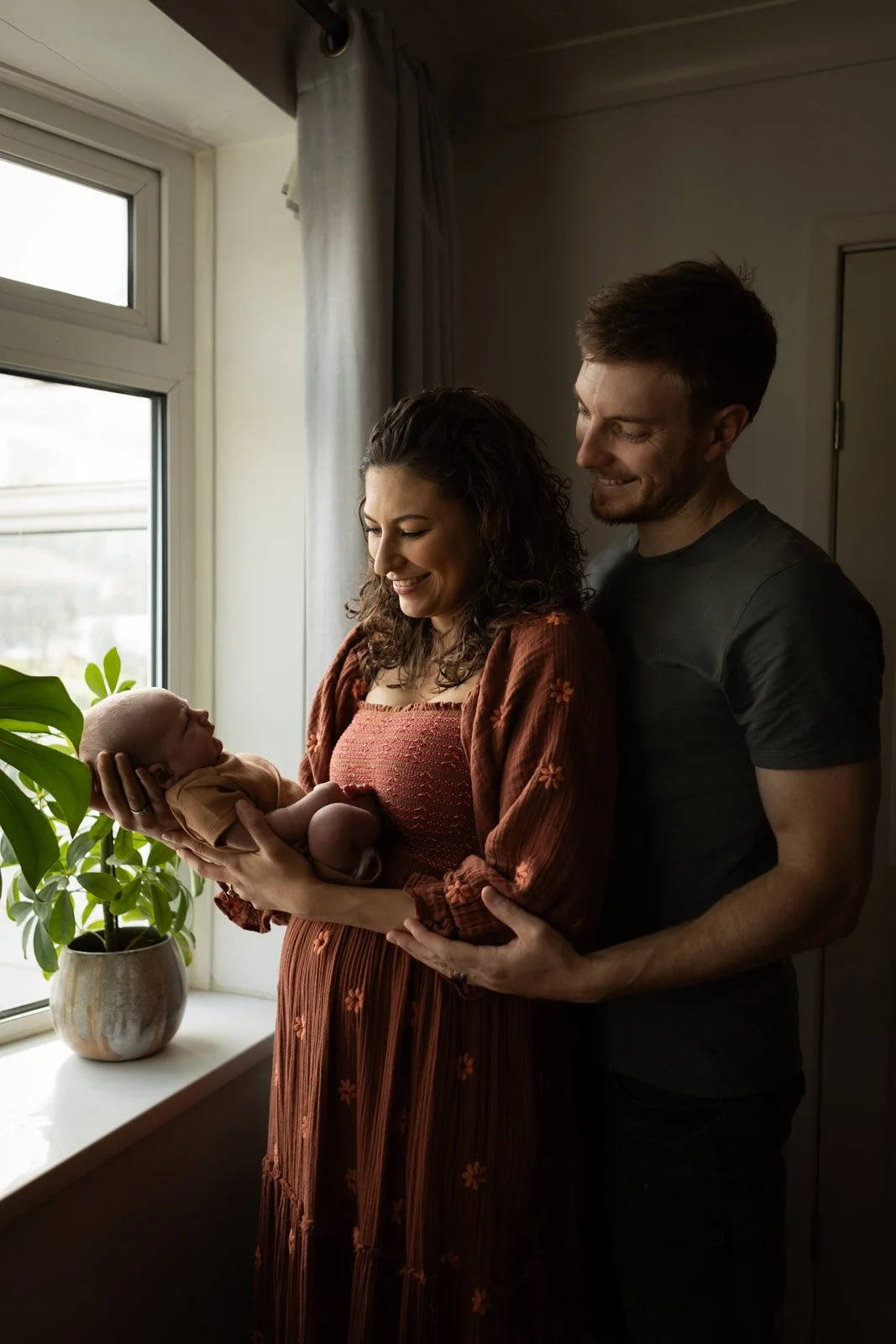 newborn baby held by smiling parents in natural window light
