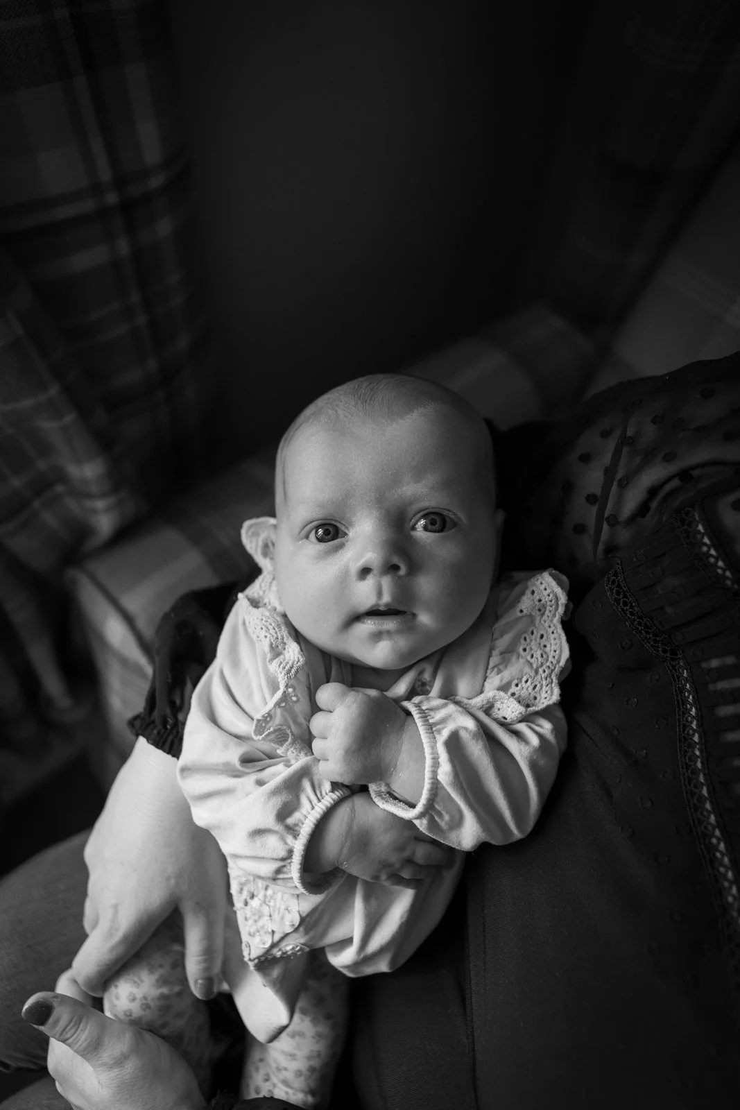 newborn baby girl clenches fists whilst held in light by mother