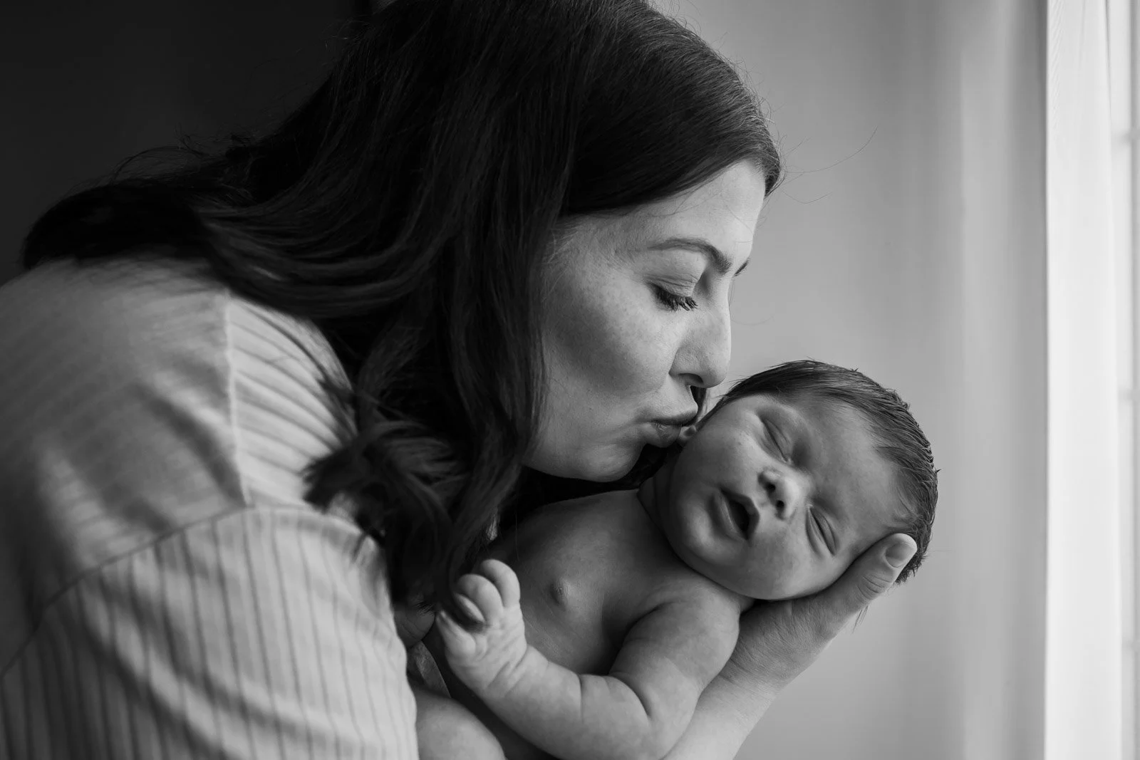 mother leans down and places kiss on baby sons' cheek as he sleeps