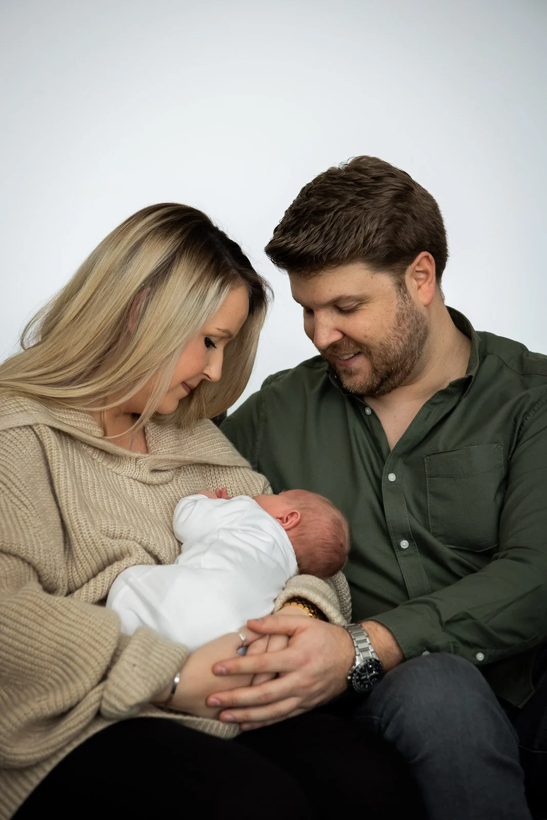 mum and dad gaze down at new son whilst smiling