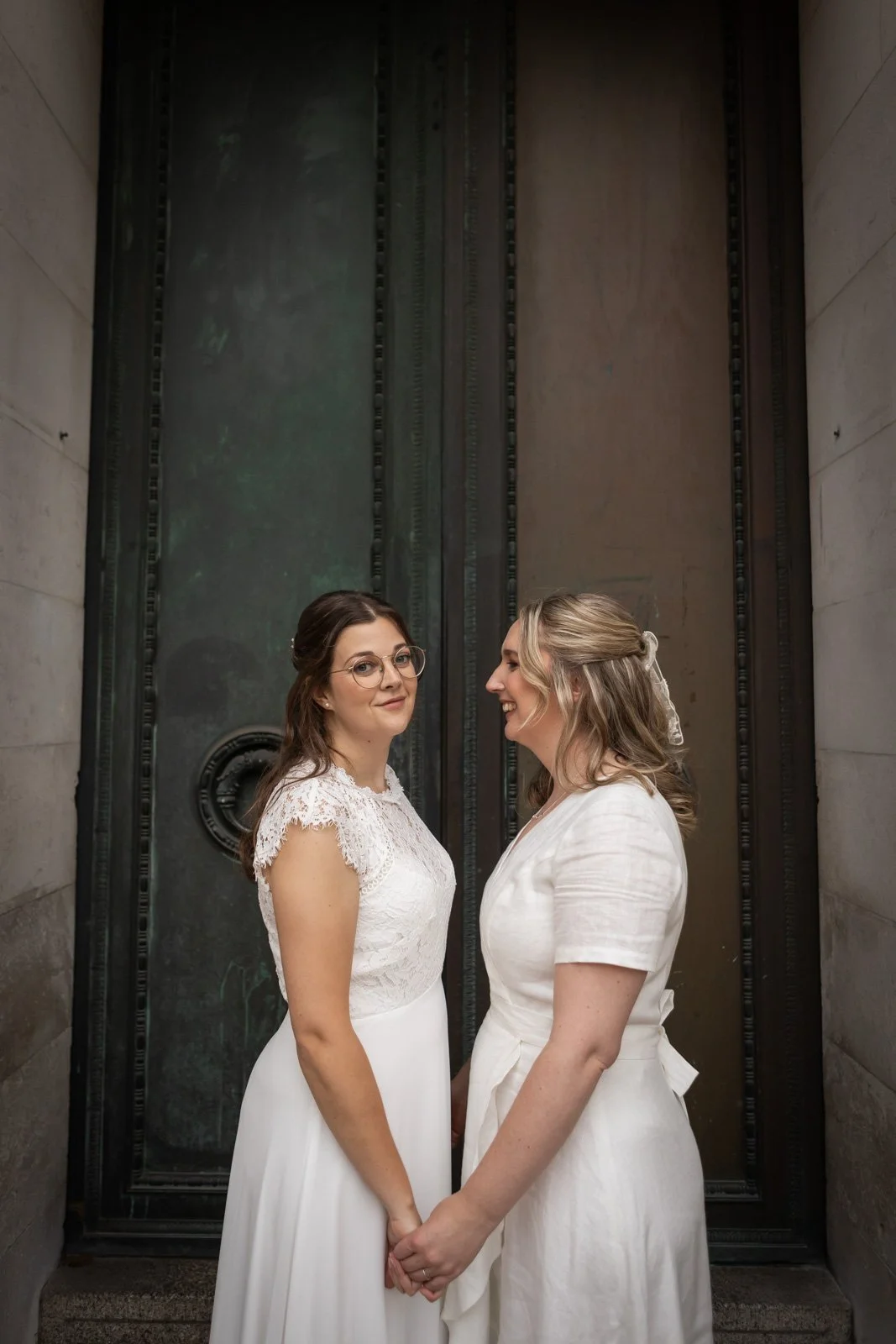 same sex couple hold hands in doorway of City Hall, Cardiff in wedding dresses