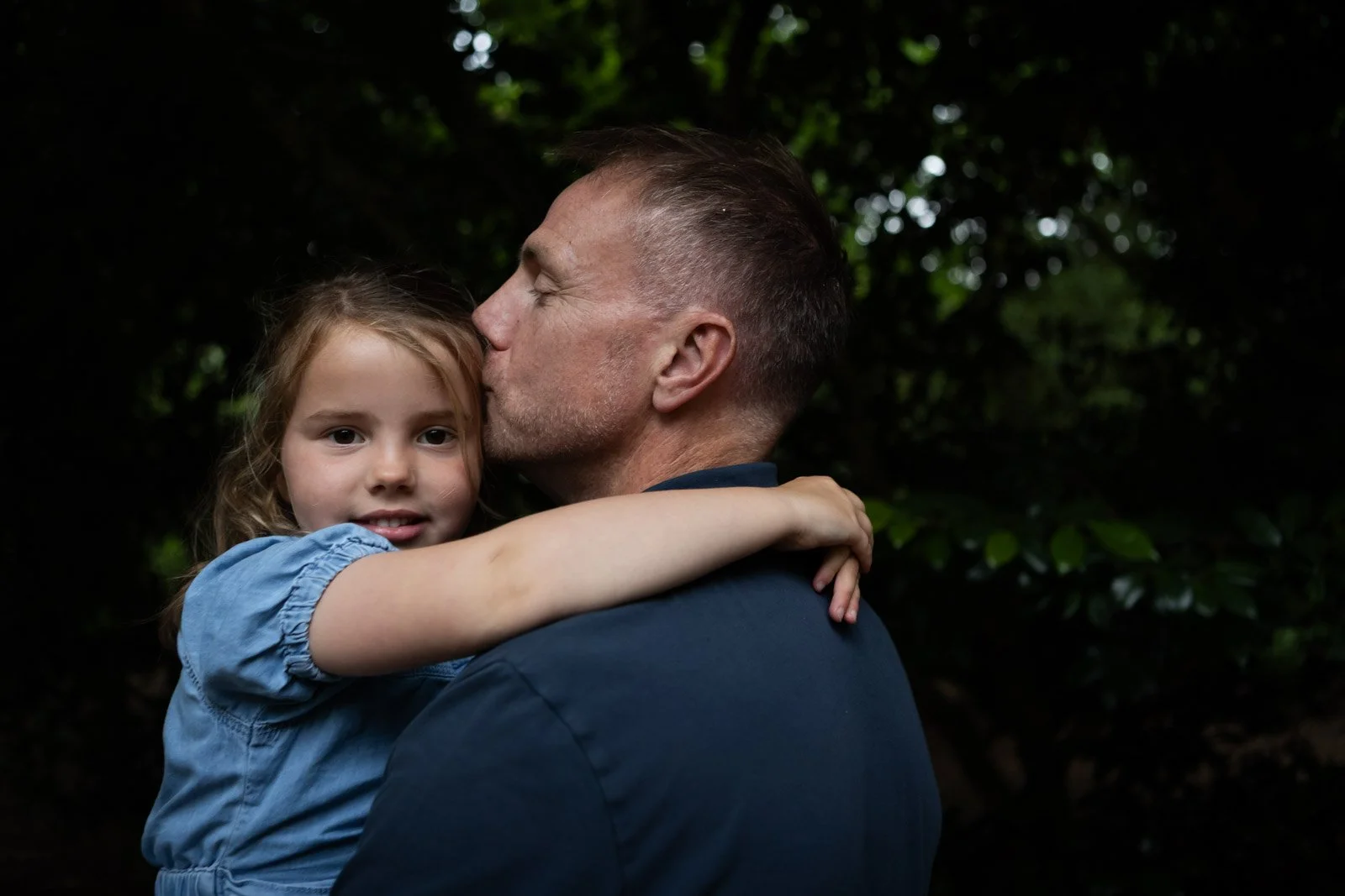 dad of family holds daughter and places kiss on her head
