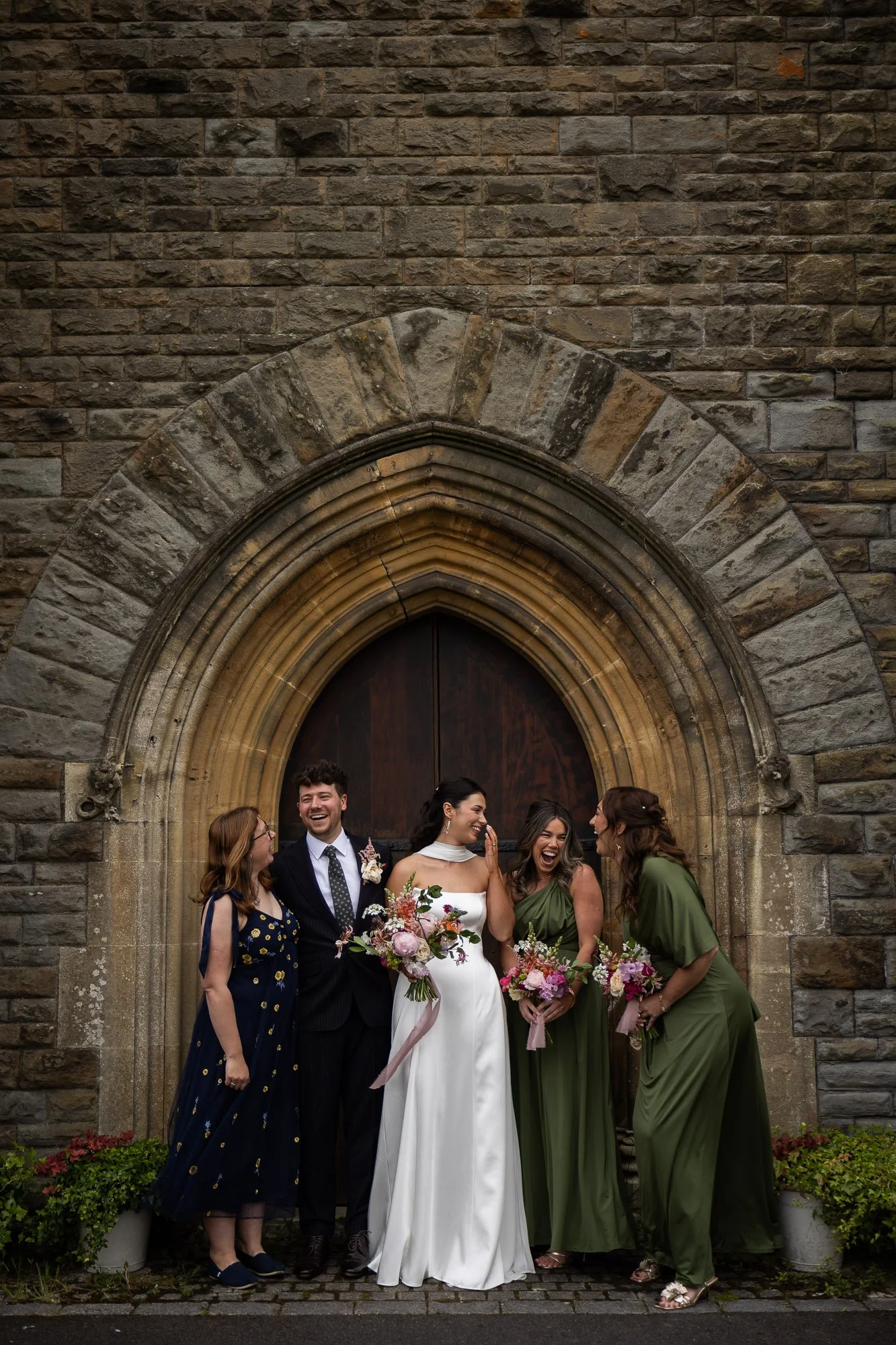 Bride giggles with bridal party in doorway or church in Cardiff