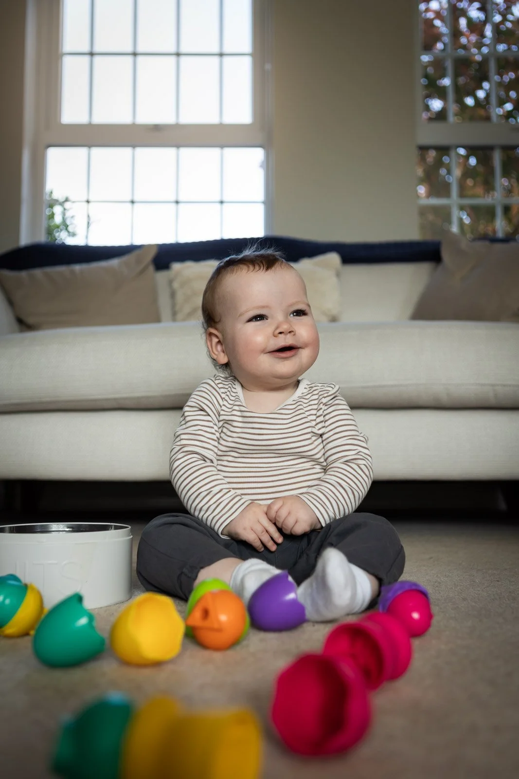 baby looks up and smiles at family whilst playing with coloured balls in lounge at home