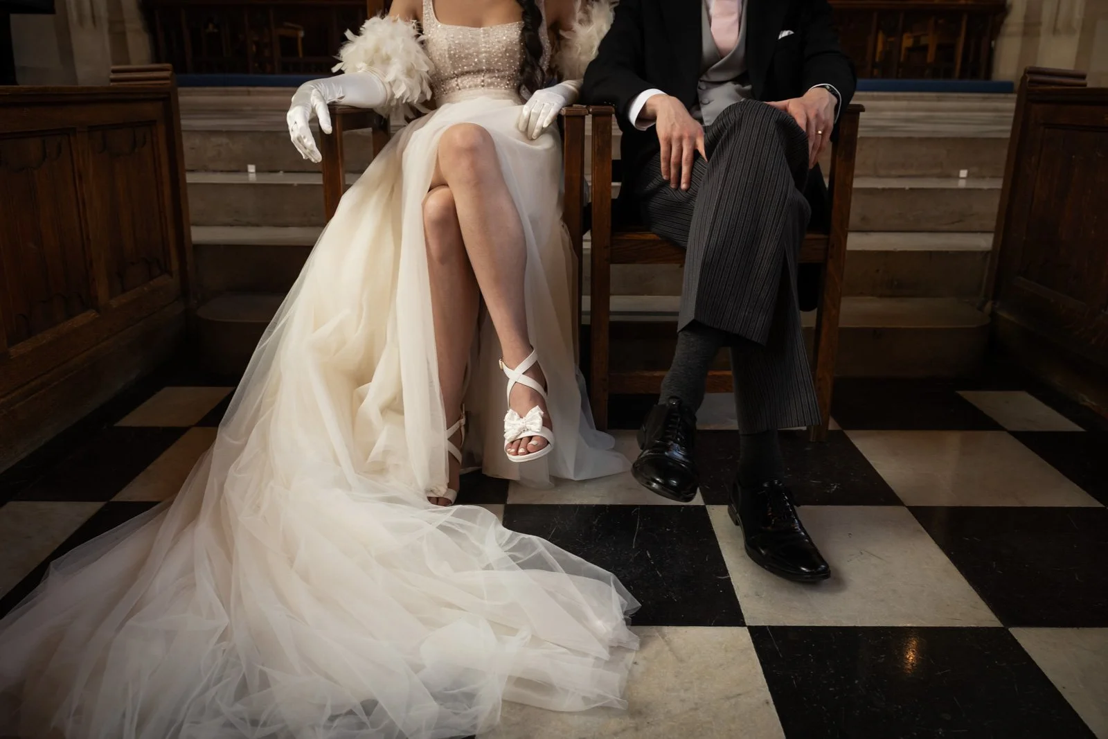 bride and groom sat in chairs in church. Photograph from waist down highlighting wedding dress
