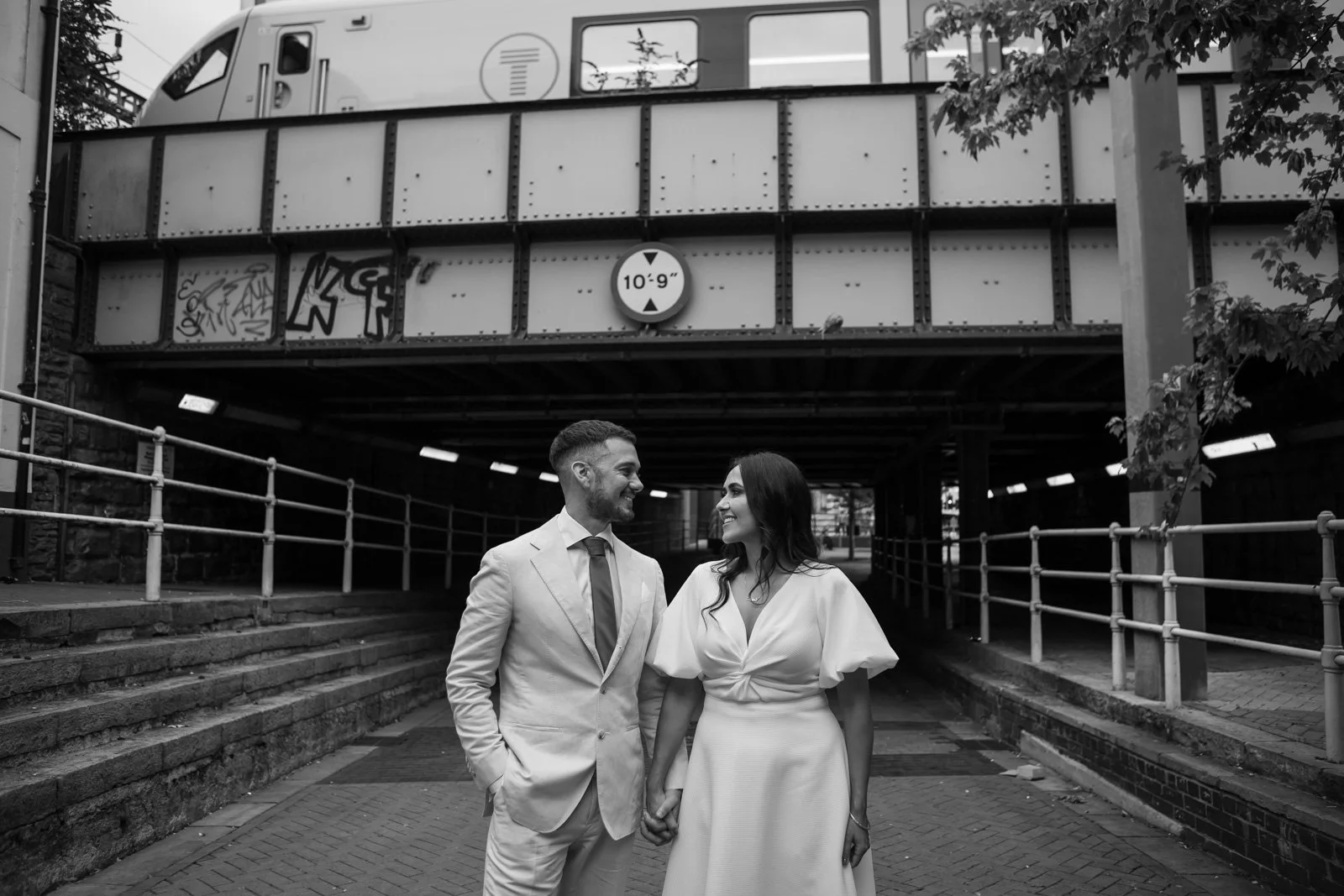 Bride and groom close to Cardiff train station hold hands on road way beneath railway bridge 