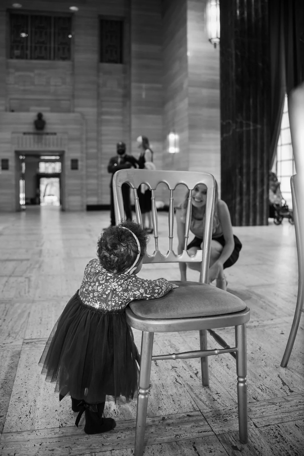 little girl peers through chair at her mother