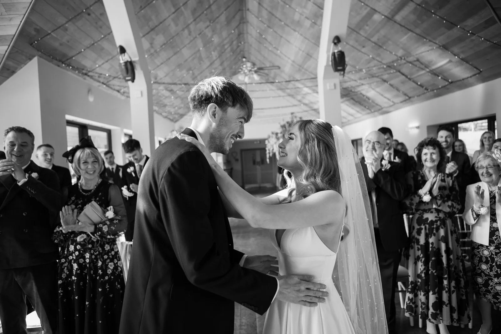 bride and groom hold each other as they get married and smile whilst guests clap