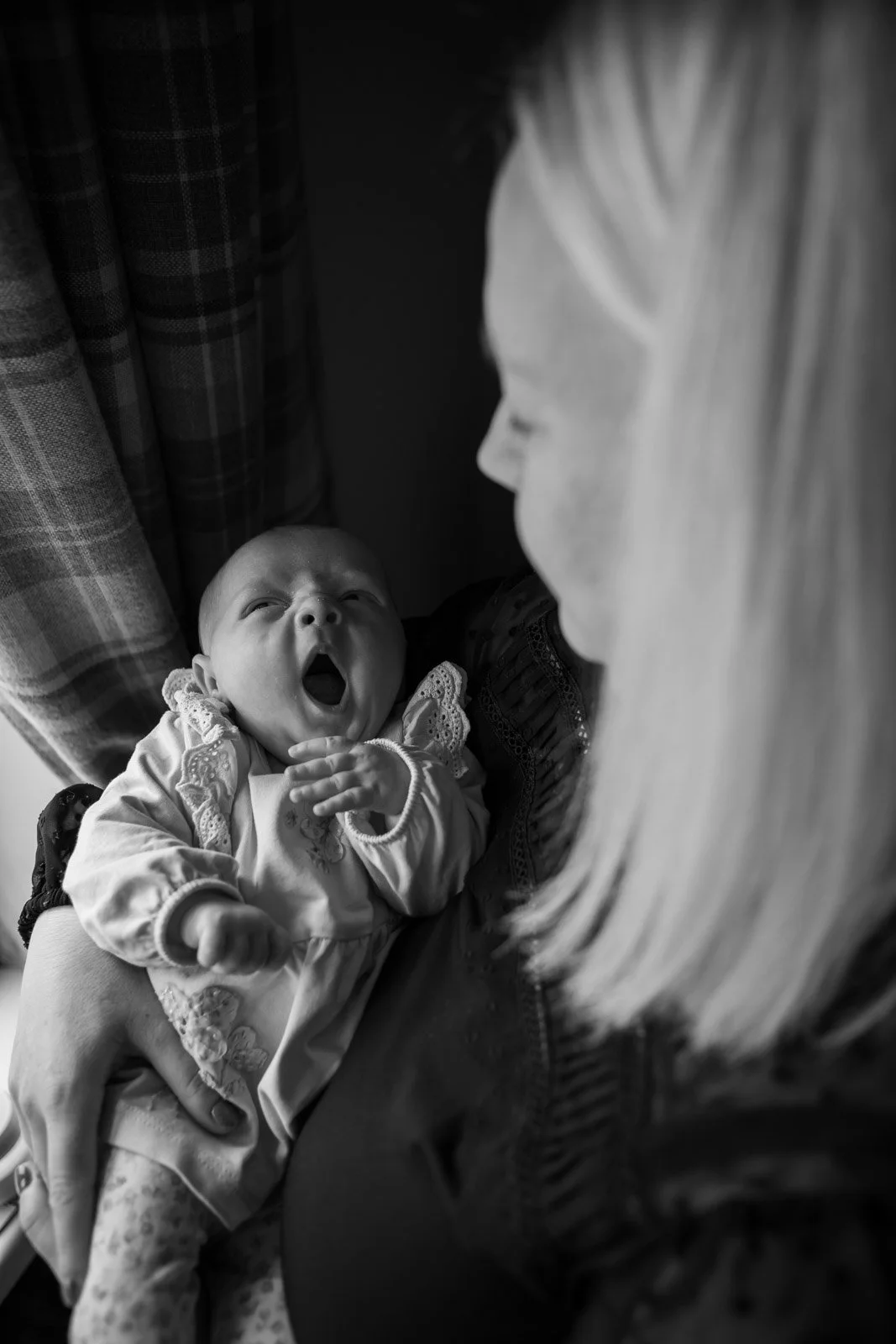 yawning baby girl held by mother who looks down at her