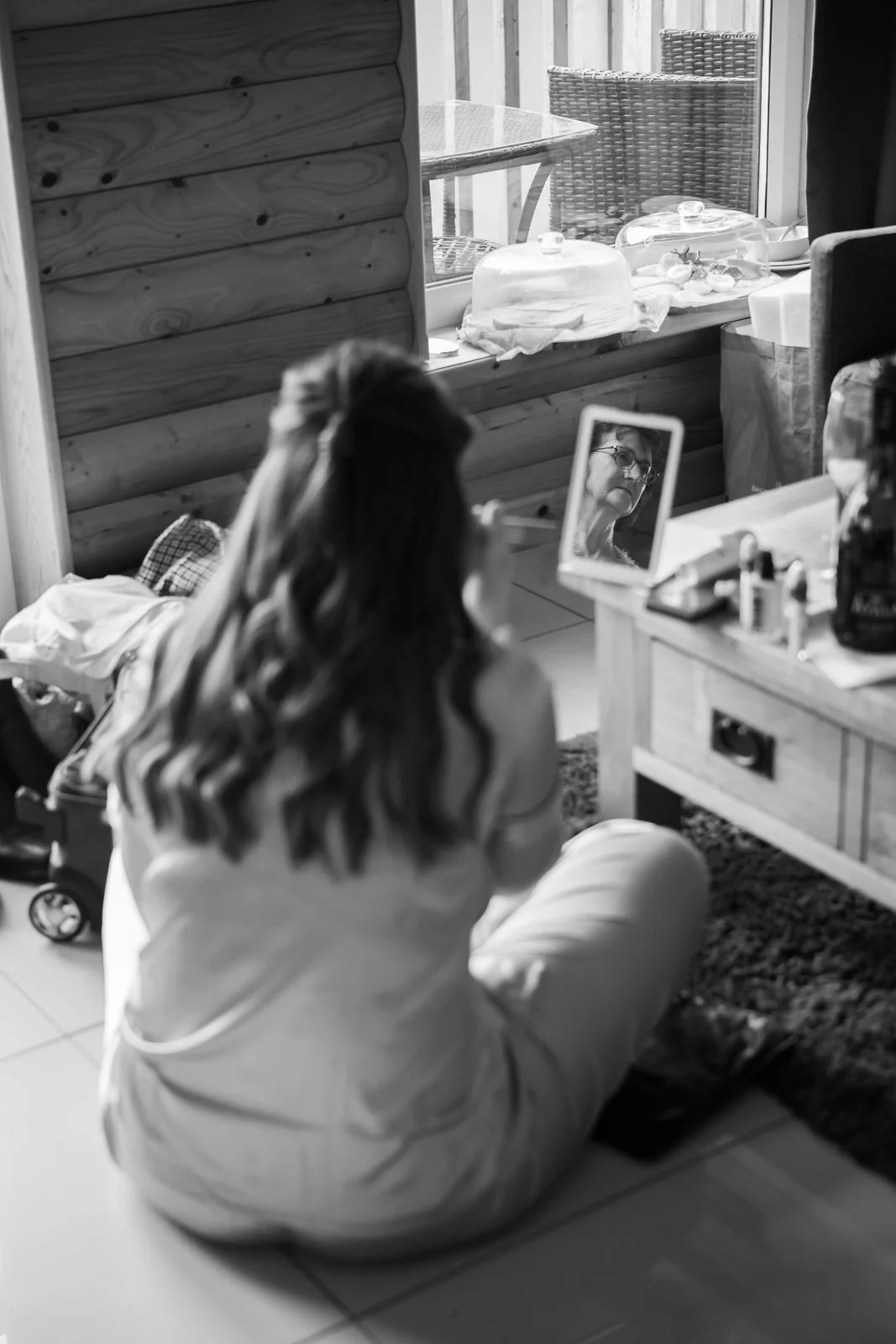 mother of the bride captured in small mirror as bridesmaid does make up