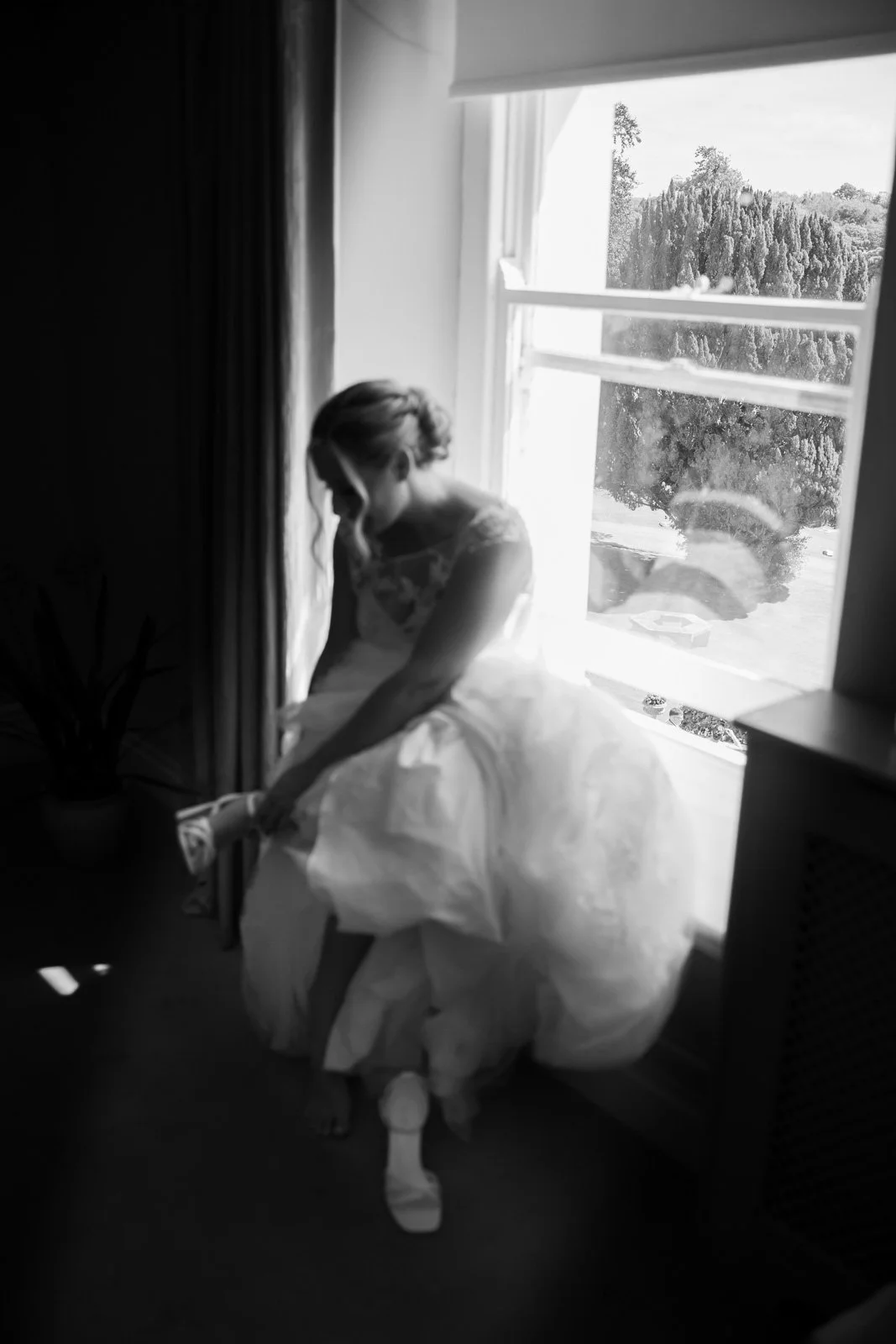 bride puts on wedding shoes in window light at Court Colman Manor