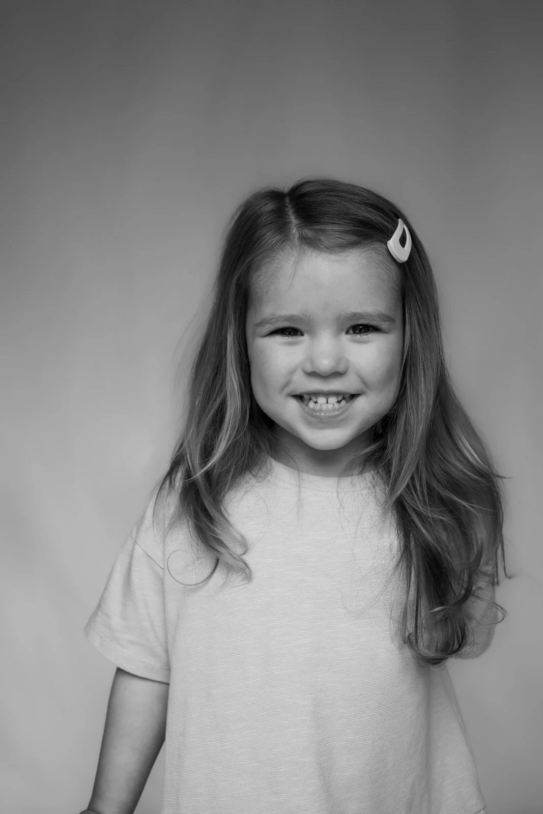 young girl stands and smiles at camera against white backdrop