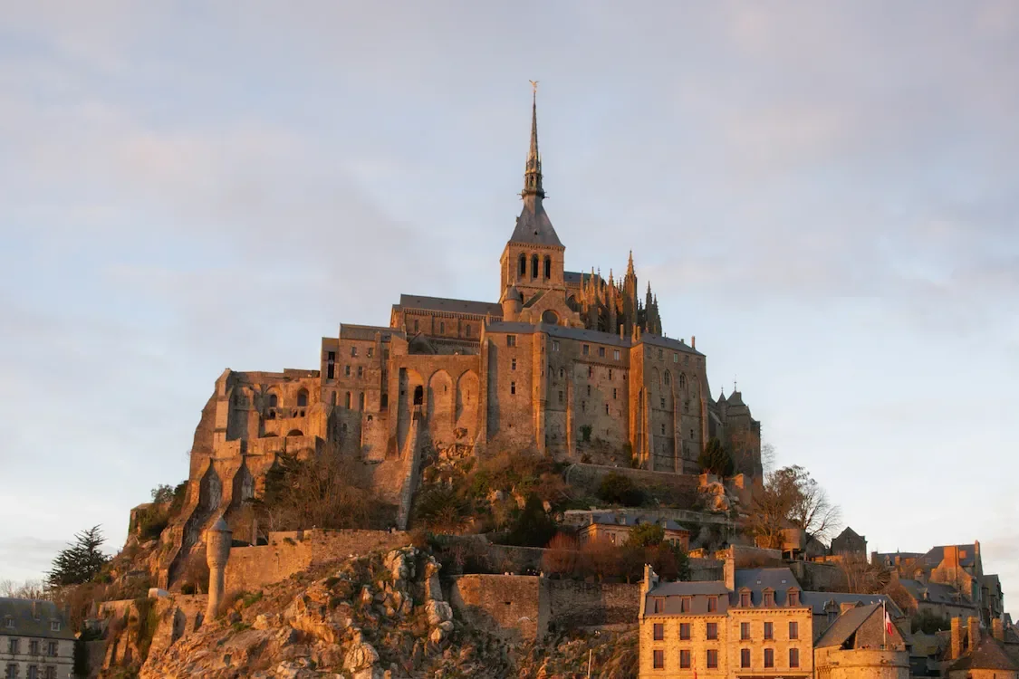 View of Mont Saint-Michel, a historic island monastery with gothic architecture, lit by sunset.