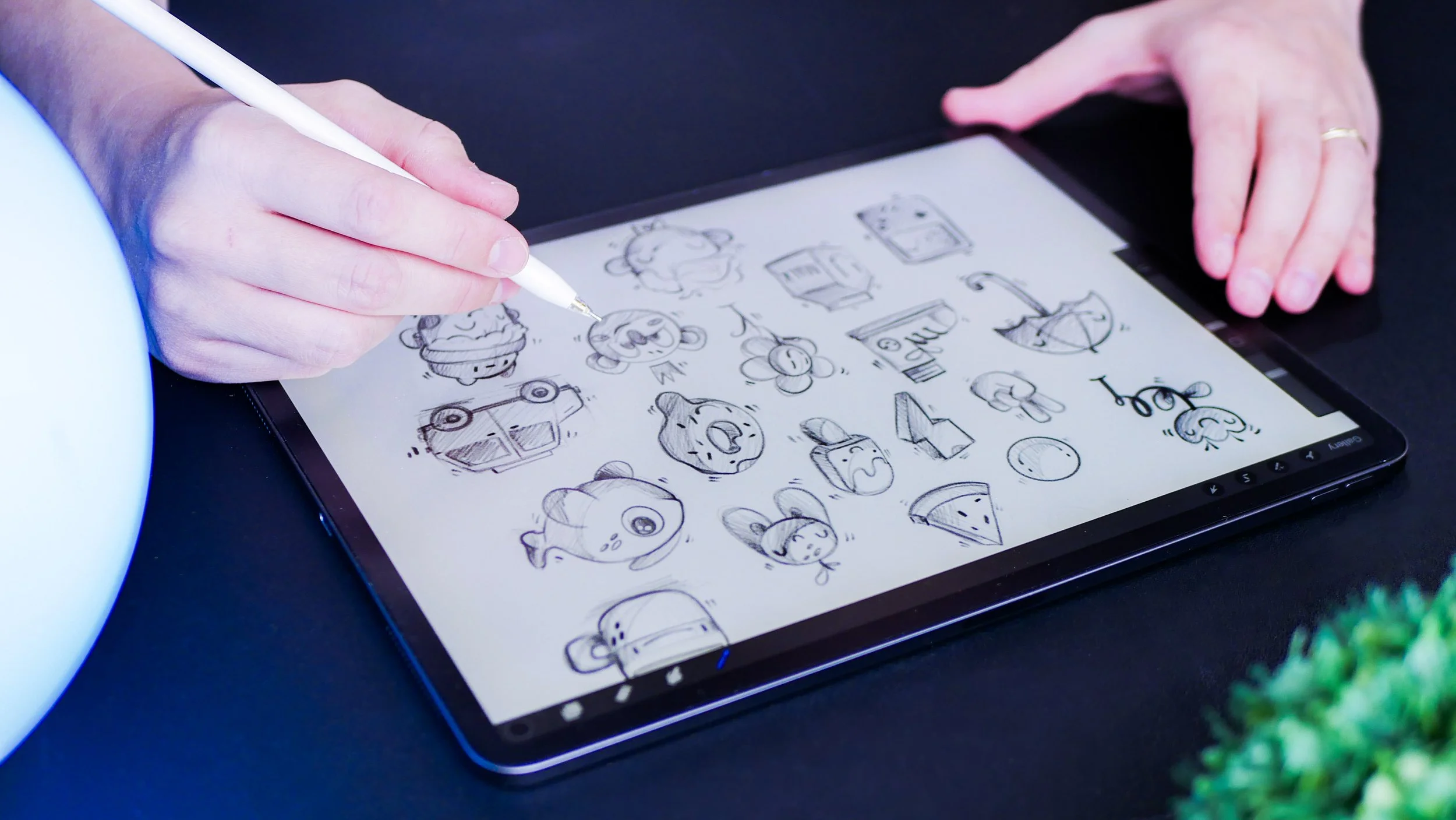Hand sketching cartoon style animals and objects on a tablet with a stylus.