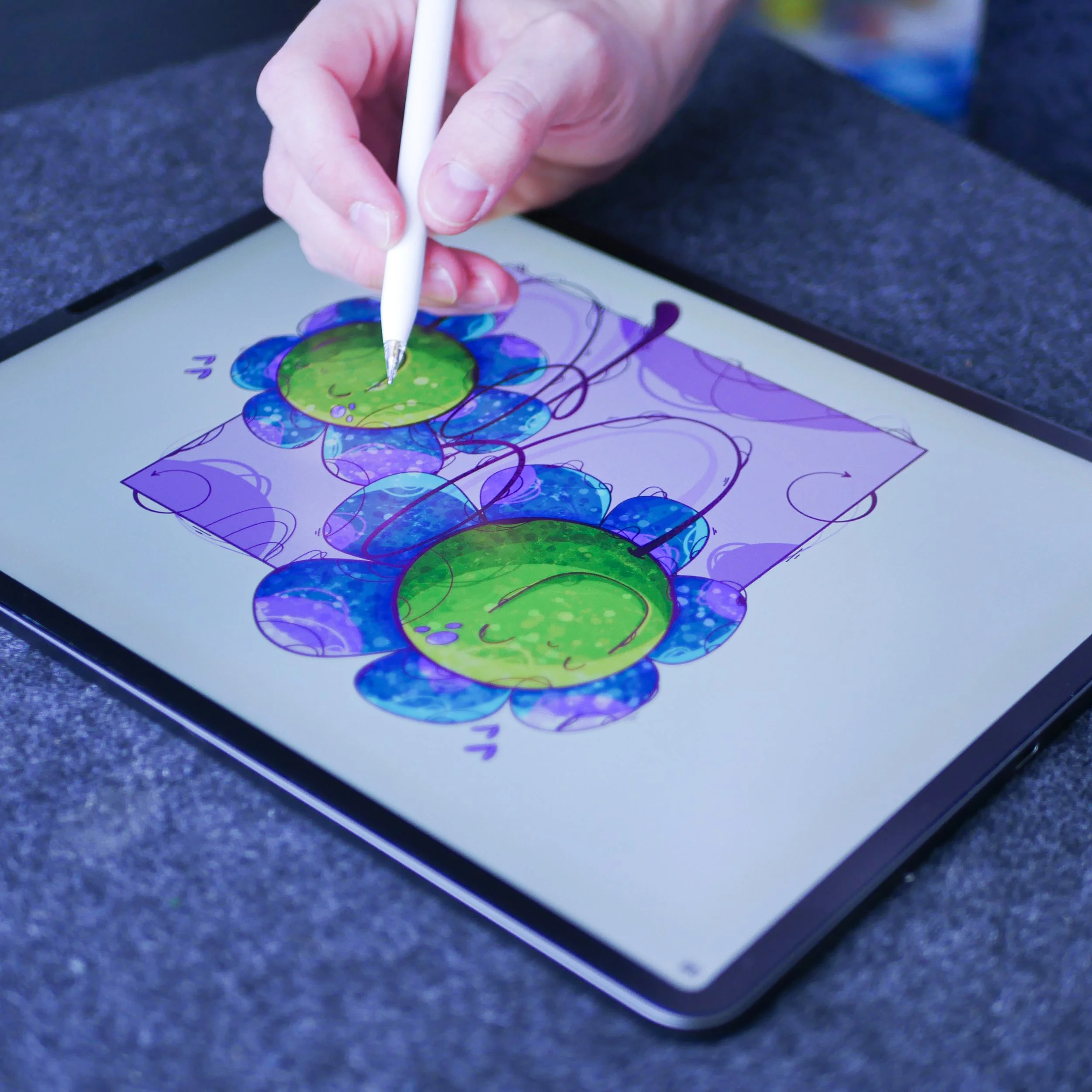 A person using a stylus to draw a colorful, abstract digital illustration of flowers on a tablet screen.