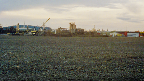 Color photo of a bleak factory. in the distance, whith a lot of bare gravel in the foreground
