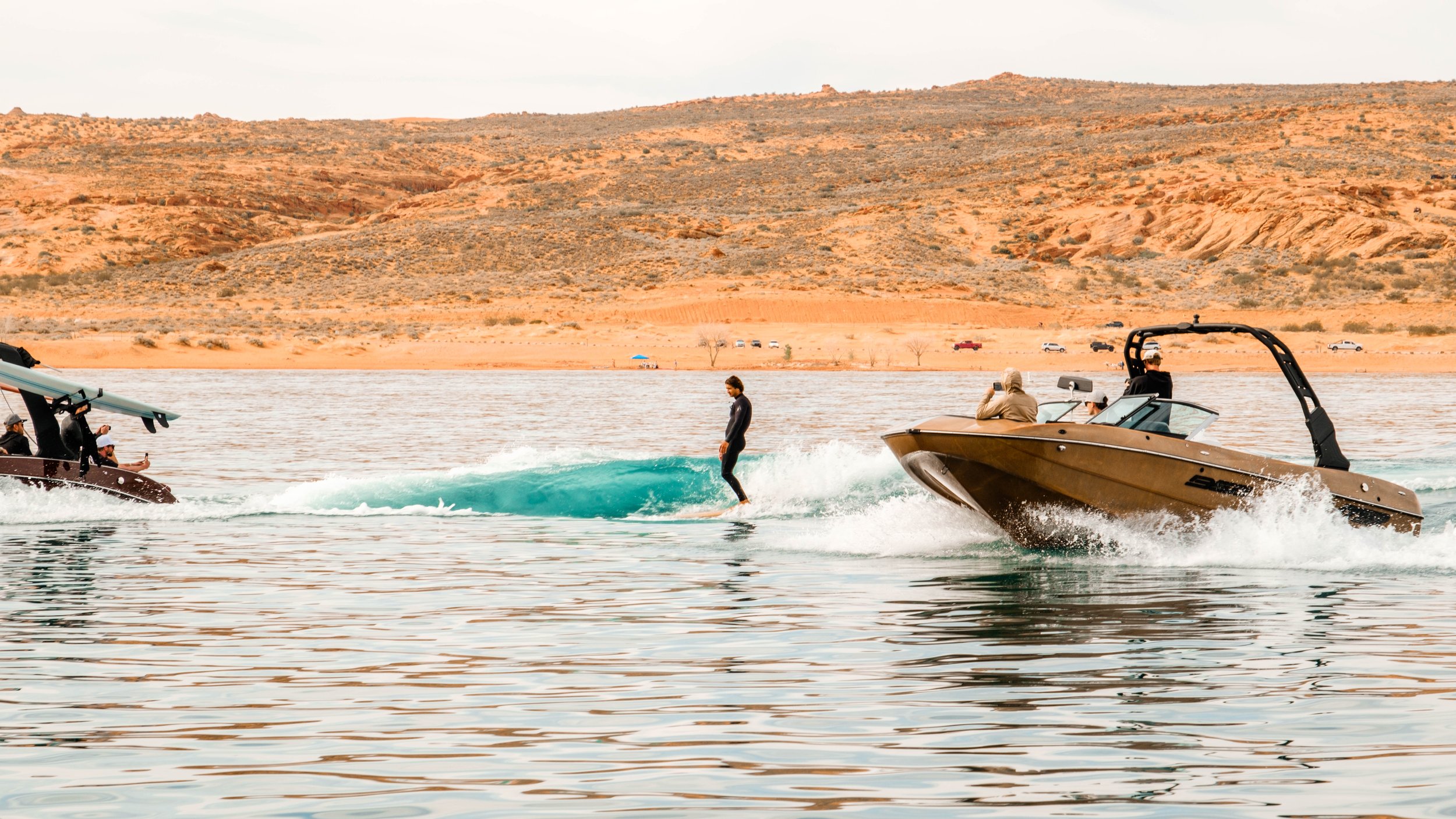A person wakeboarding behind a motorboat on a lake, with a desert landscape in the background.