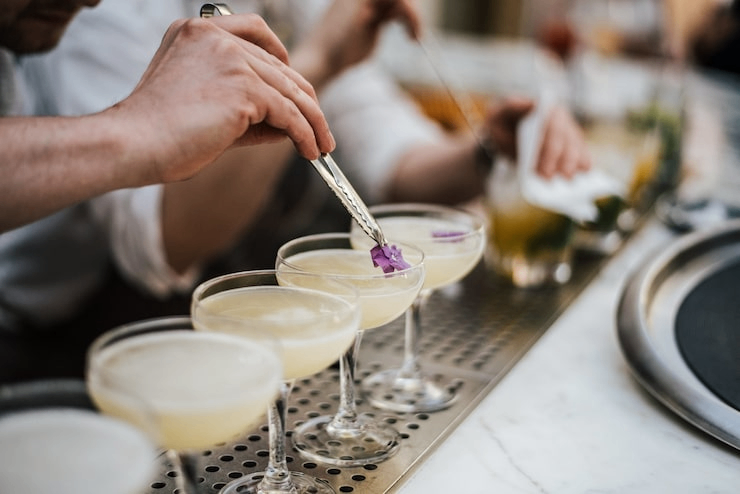 Bartender garnishing handcrafted cocktails in coupe glasses during beverage service at a catered event or cocktail reception.