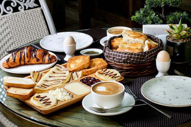 Breakfast spread with pastries, toast, eggs, and coffee served on an outdoor table.